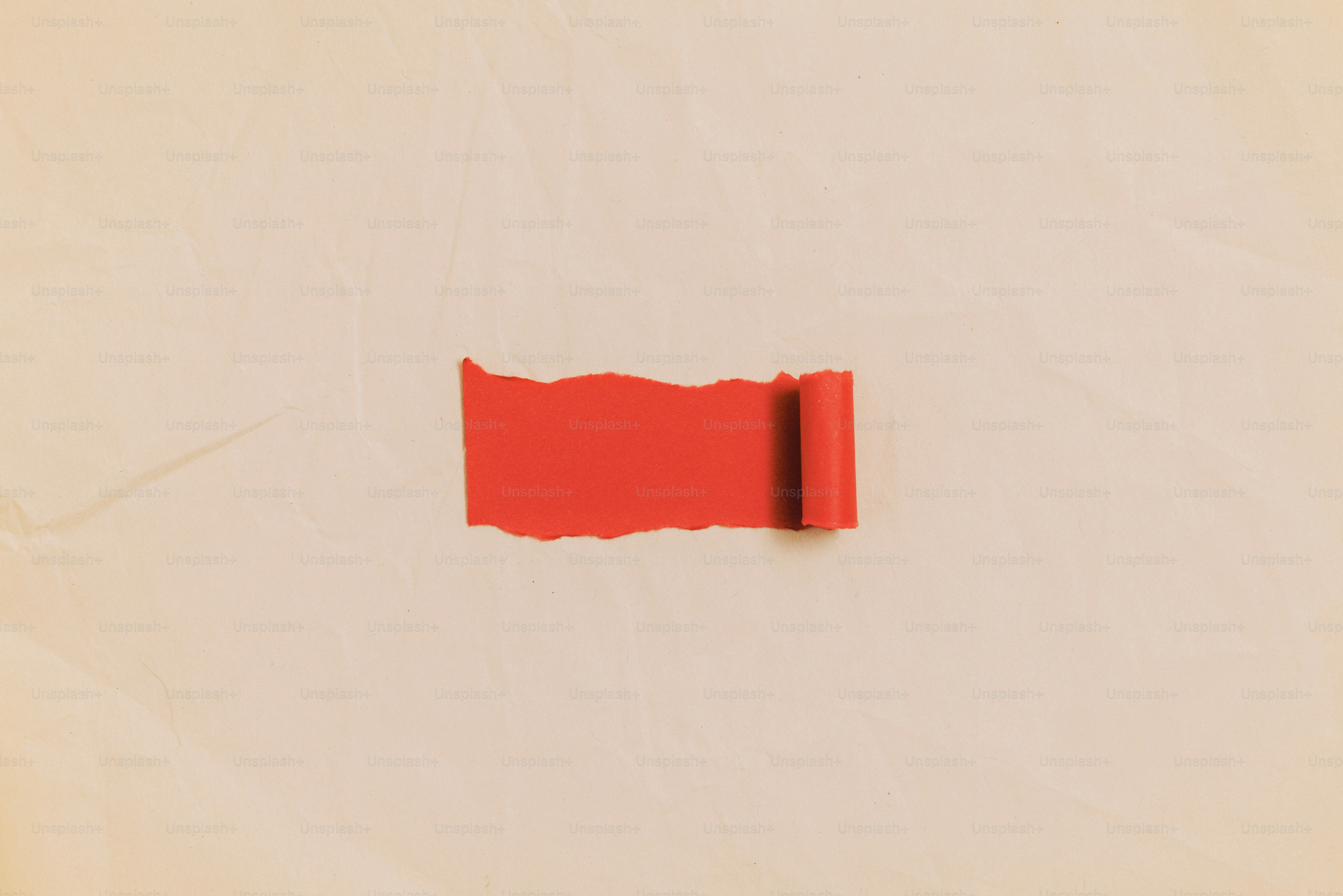Una striscia di carta rossa strappata si arricciava su uno sfondo beige