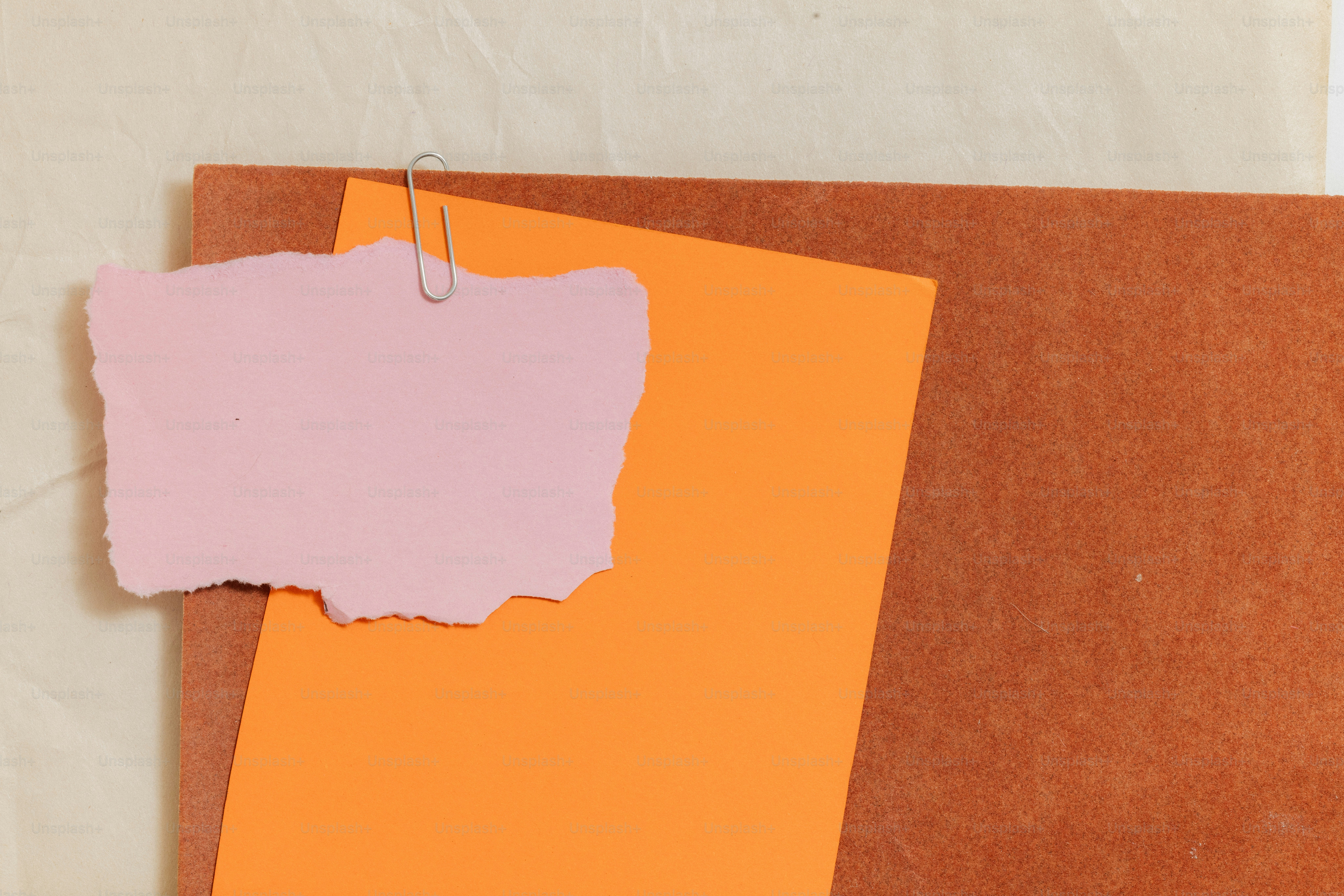 Pink torn note clipped to orange paper on brown background.