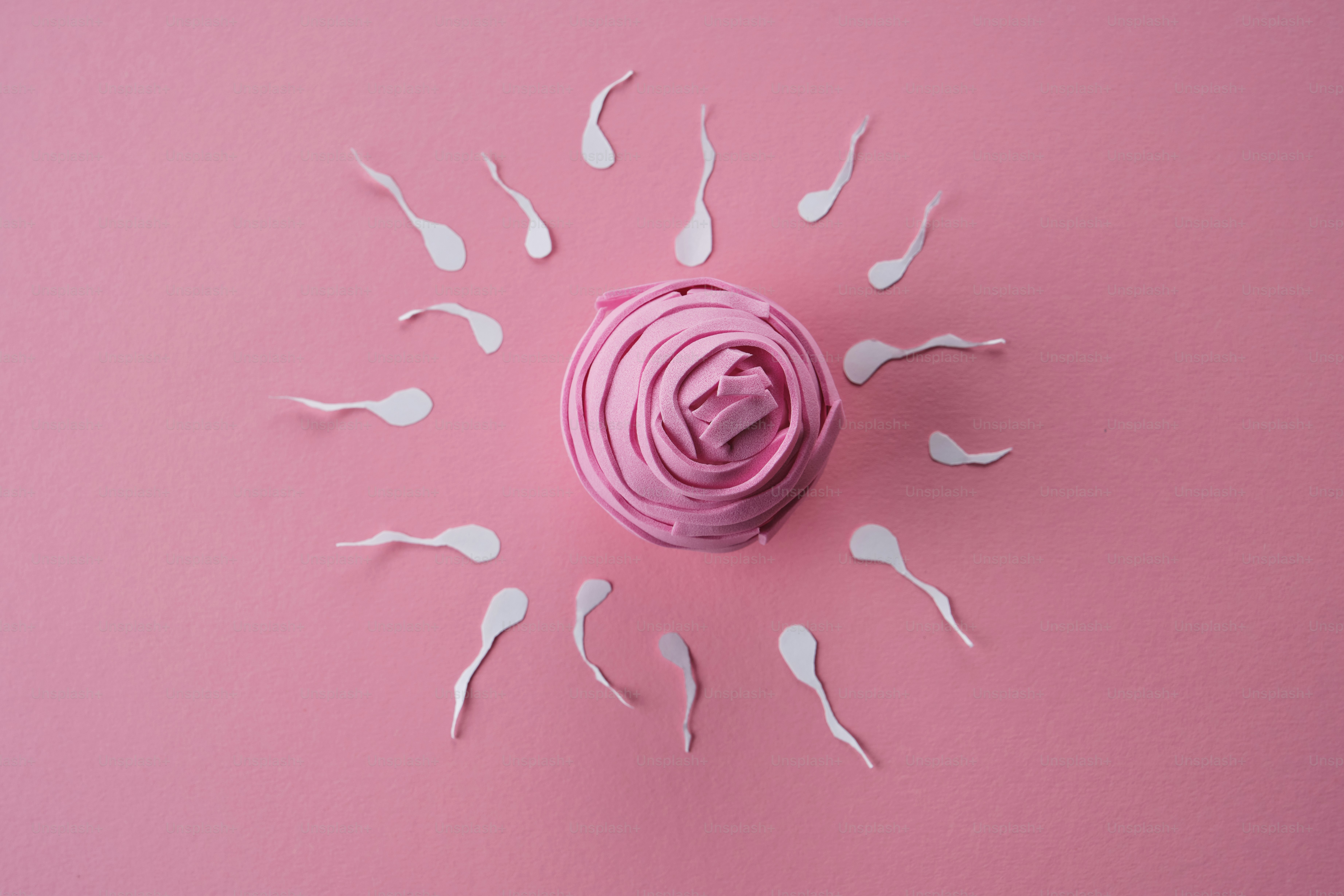 Formas blancas de esperma rodean un óvulo rosa