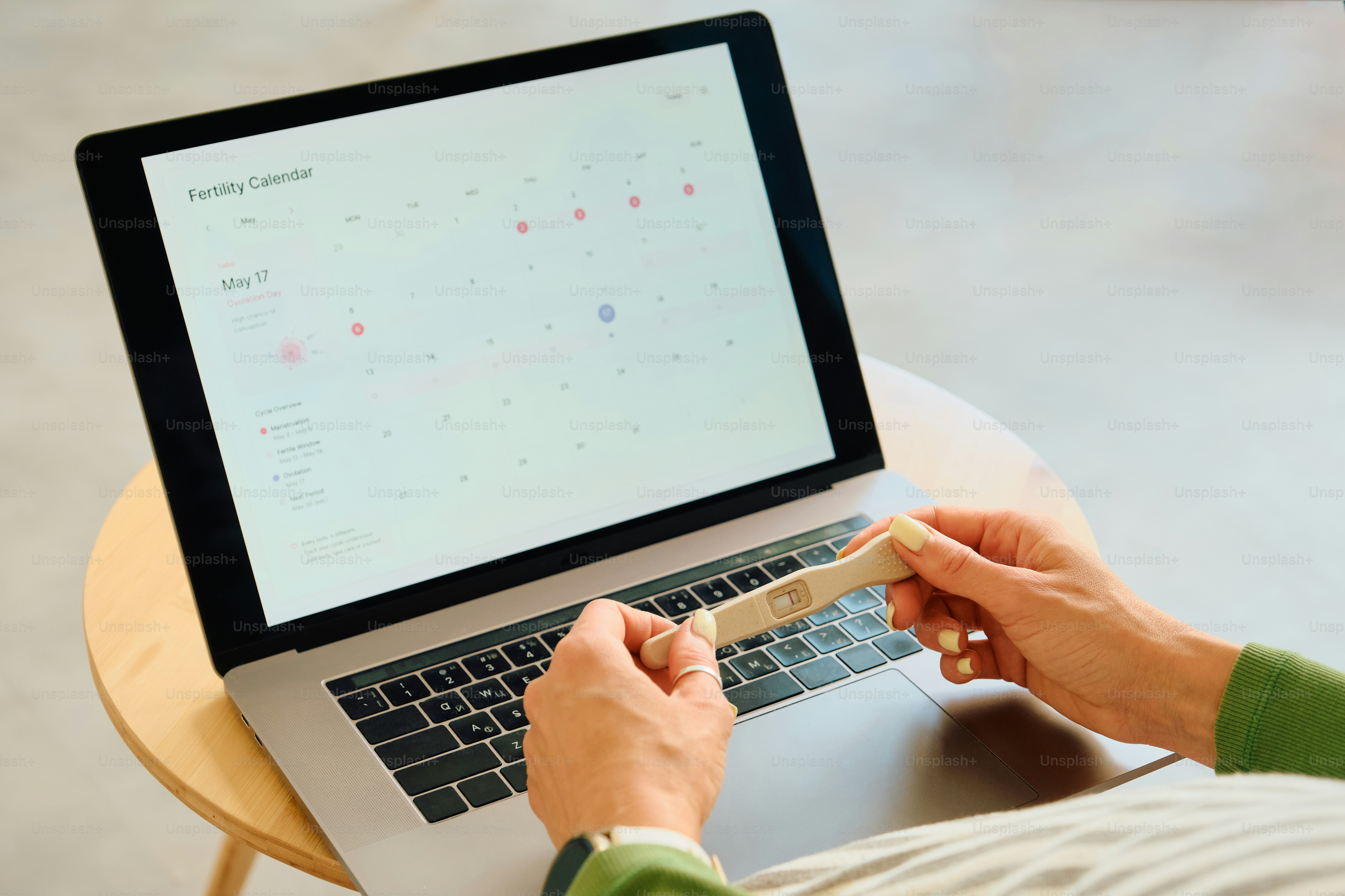 Personne tenant un test de grossesse, consultant un calendrier de fertilité sur l’ordinateur portable.