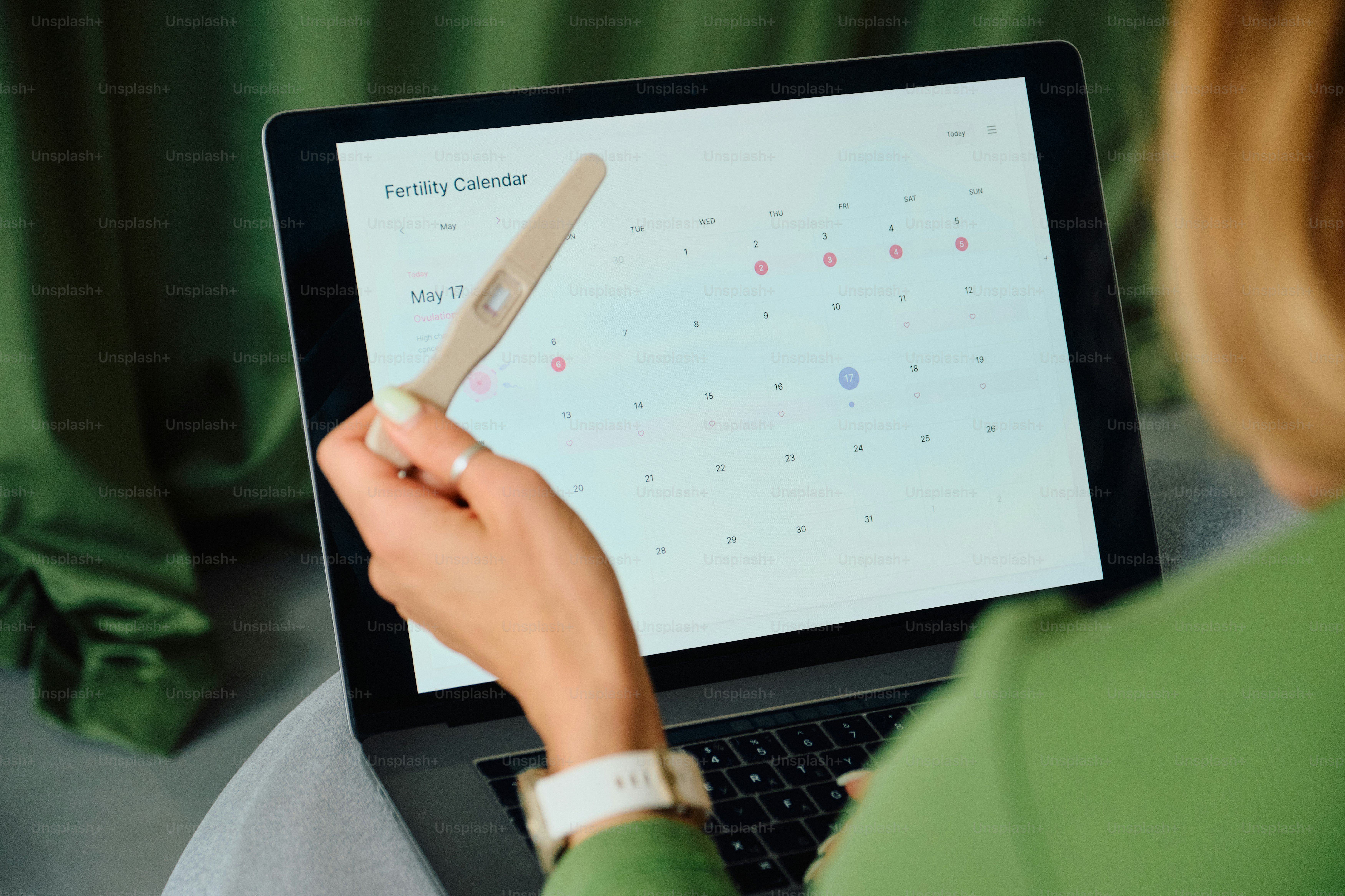 Une femme tient un test de grossesse en regardant un calendrier de fertilité sur un ordinateur portable.