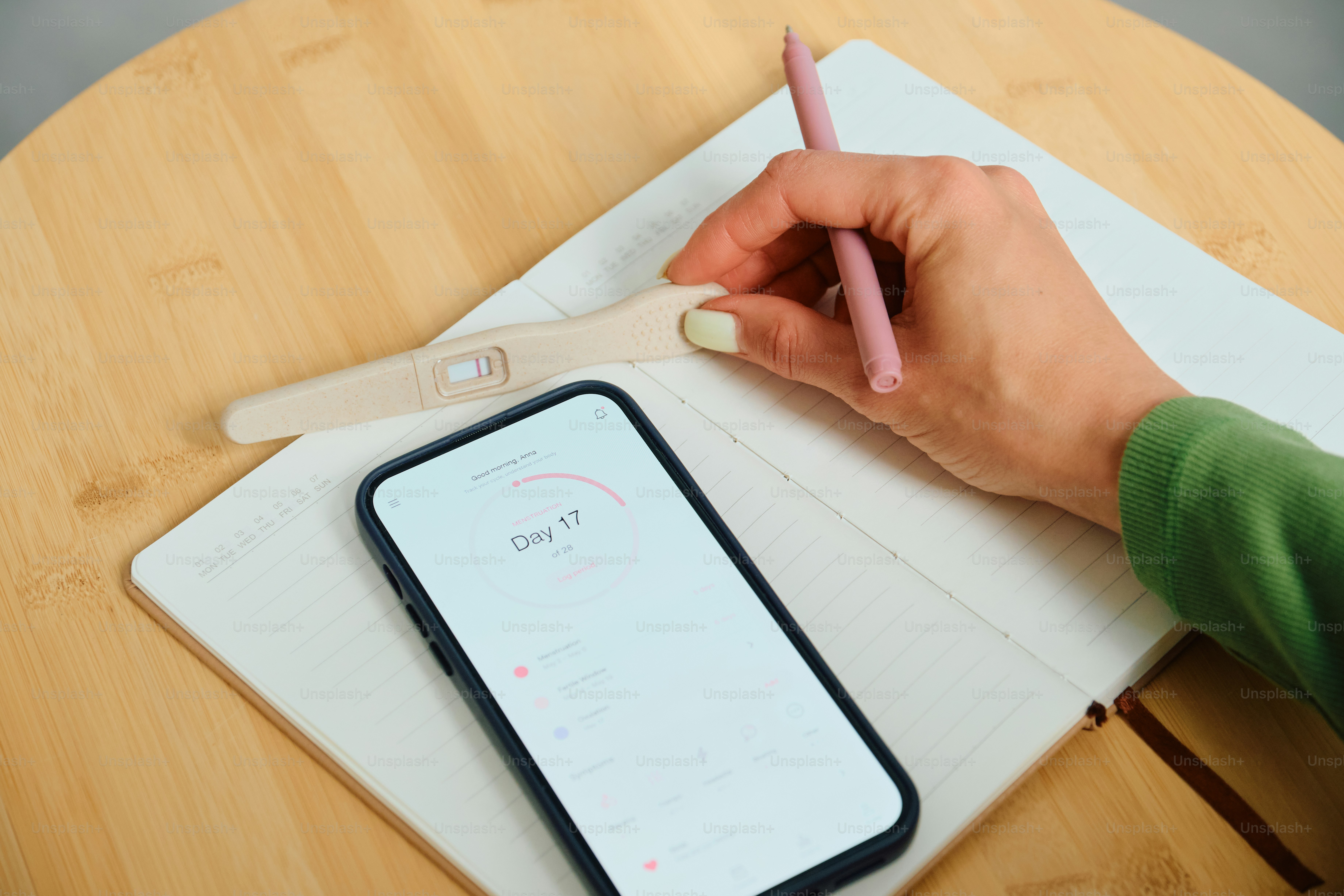 Main avec crayon, téléphone, carnet et test de grossesse.