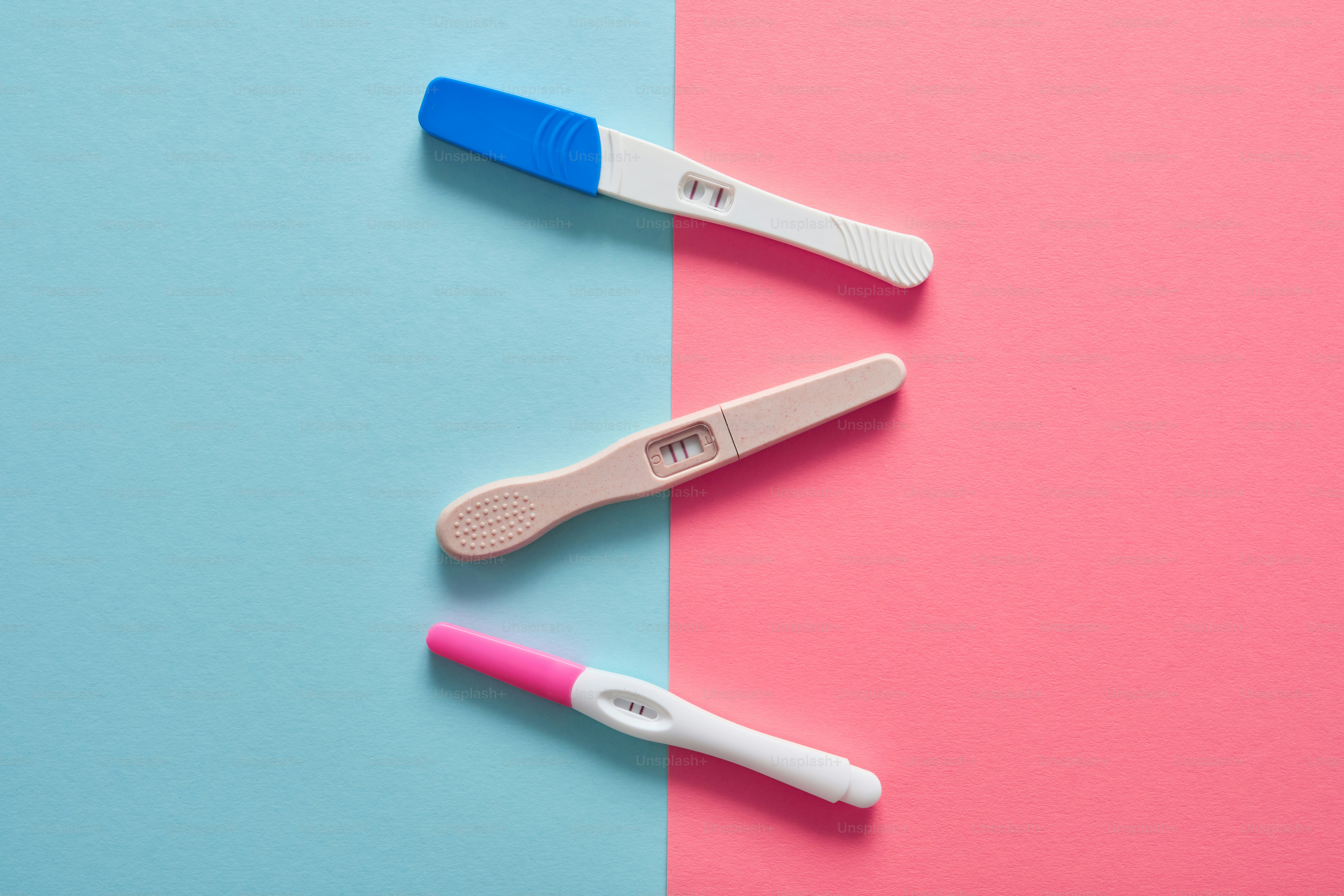 Trois tests de grossesse sur une surface fendue rose et bleue.