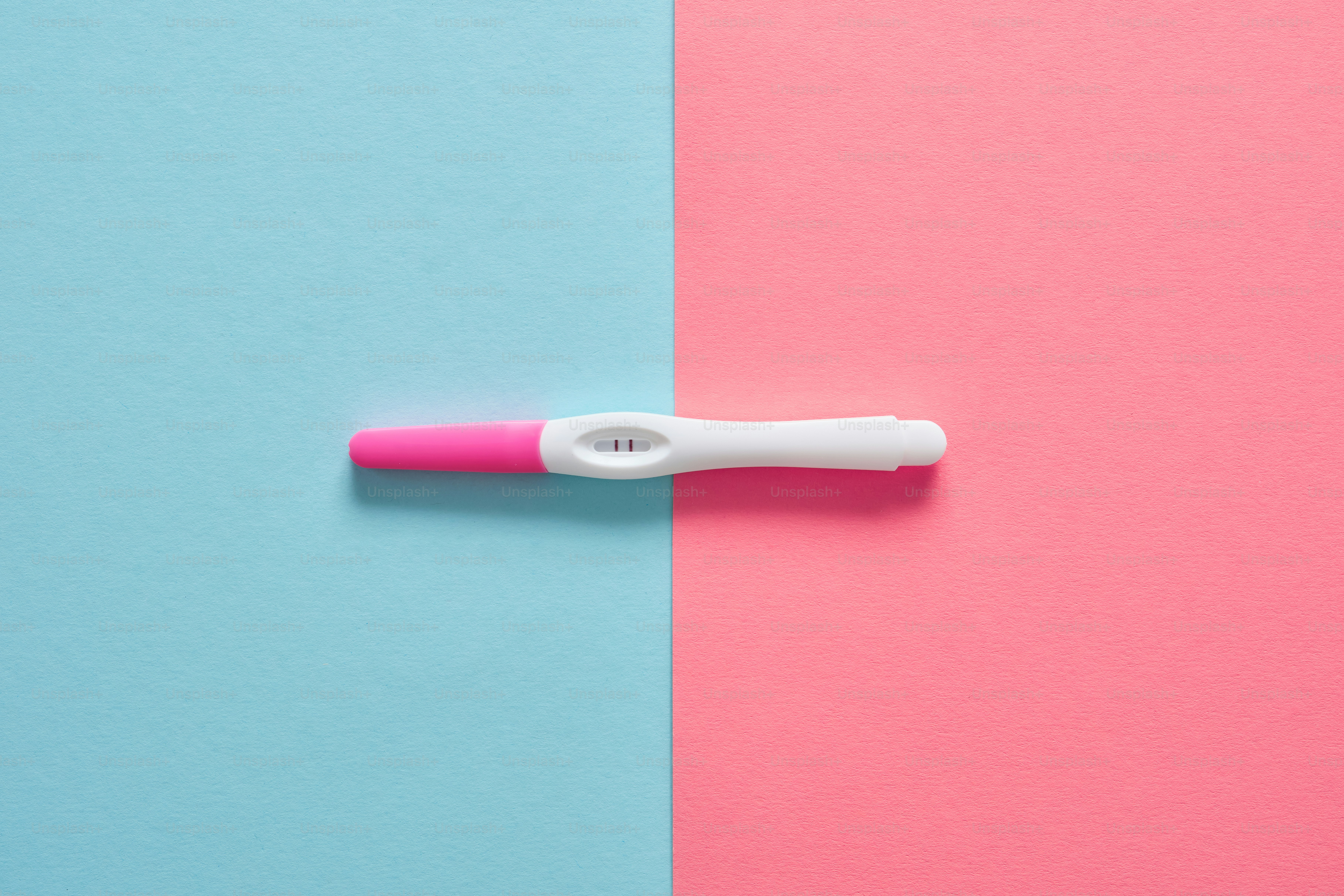 Un test de embarazo positivo sobre un fondo rosa y azul