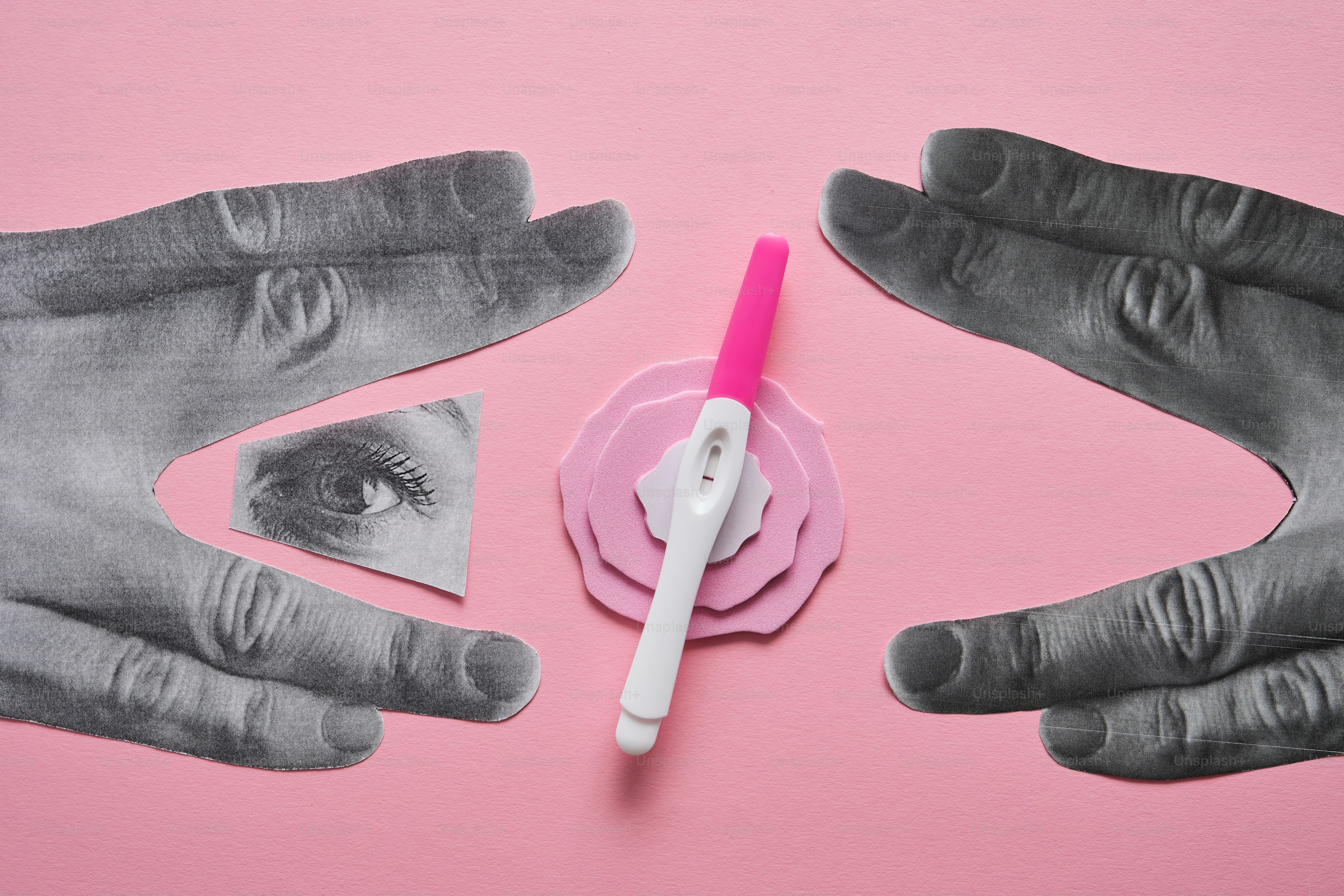 Deux mains en niveaux de gris encadrent un test de grossesse positif sur du rose.