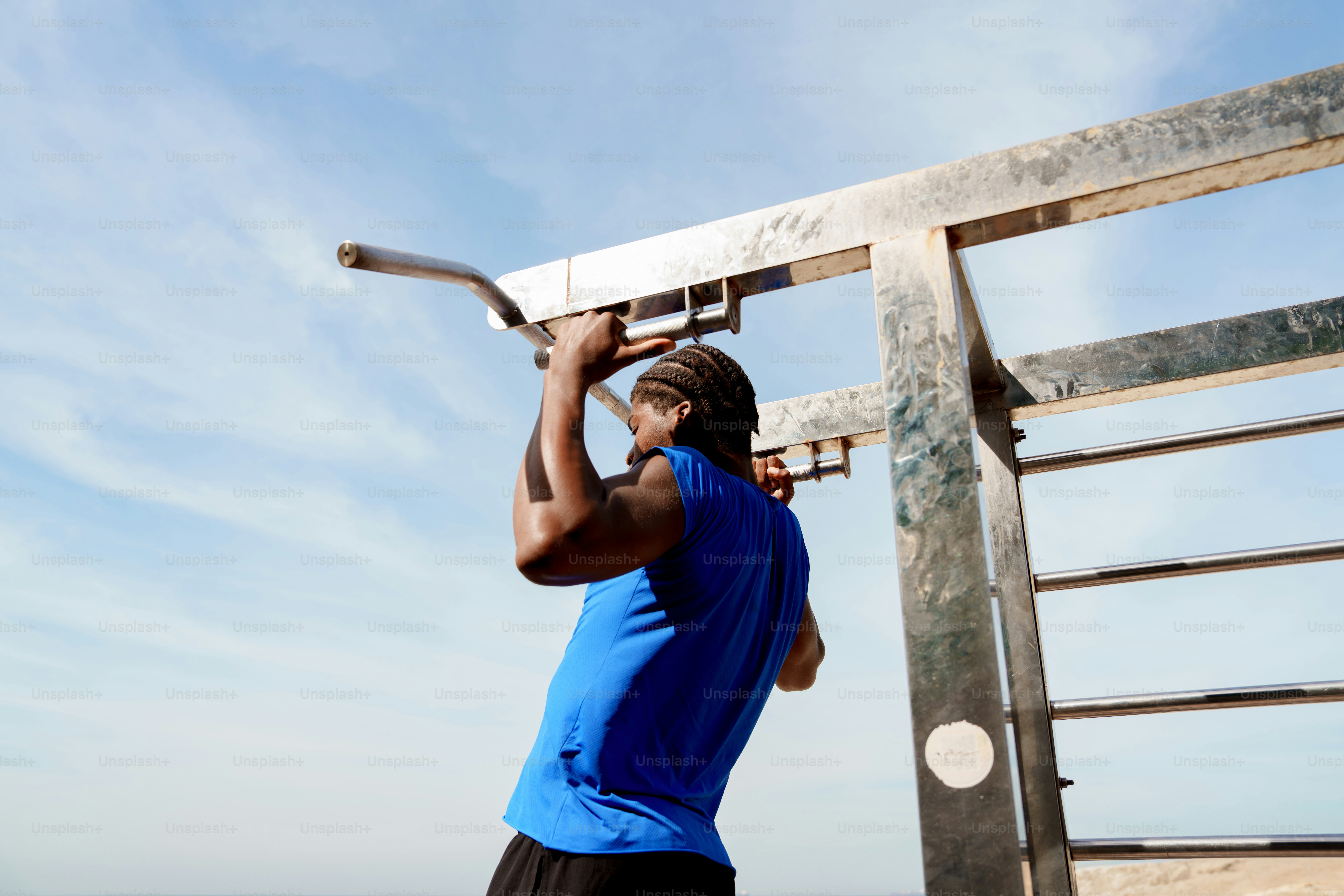 A man in a blue shirt performs a pull-up outdoors.