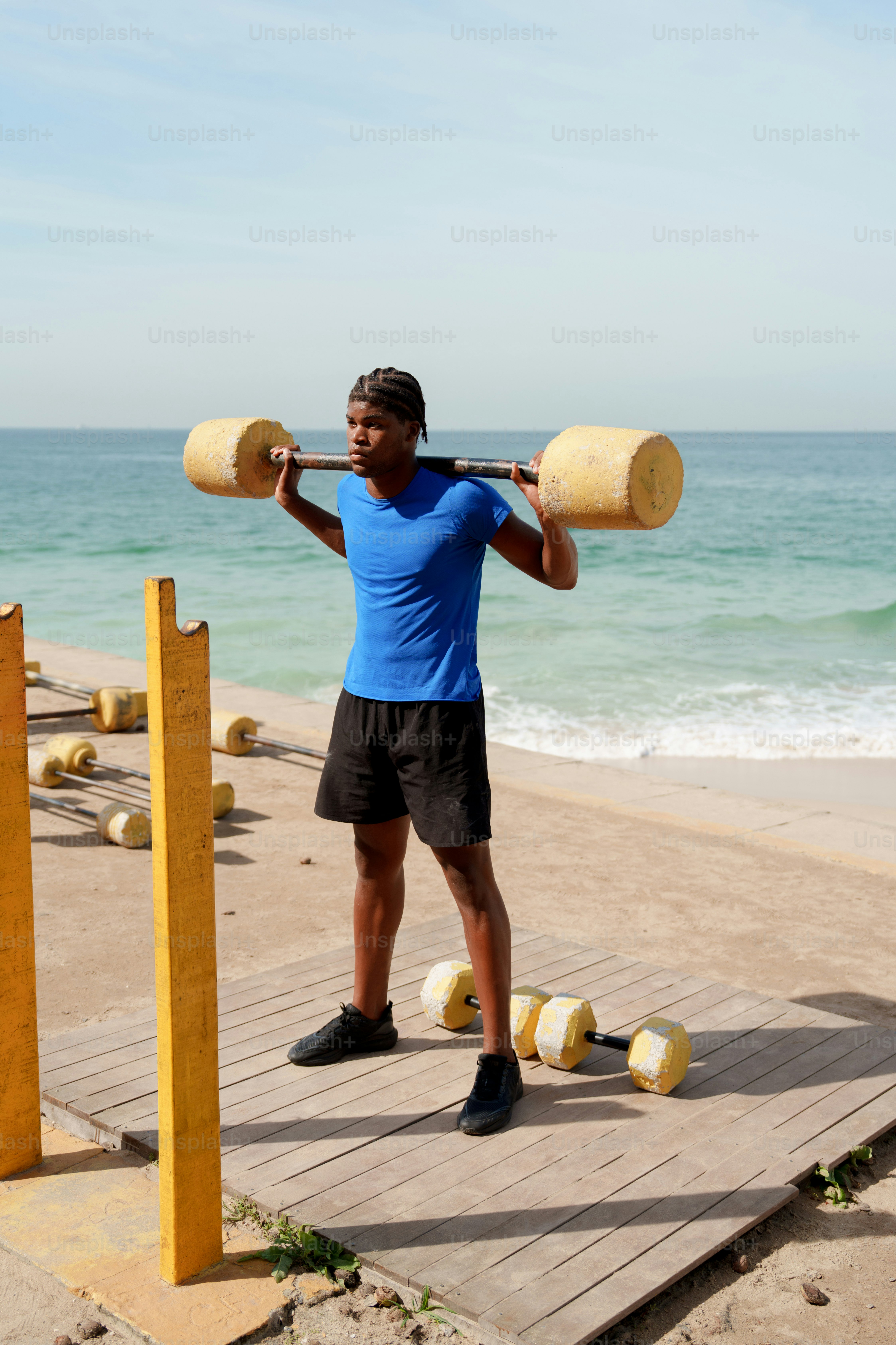 Young man exercising with a barbell by the ocean.