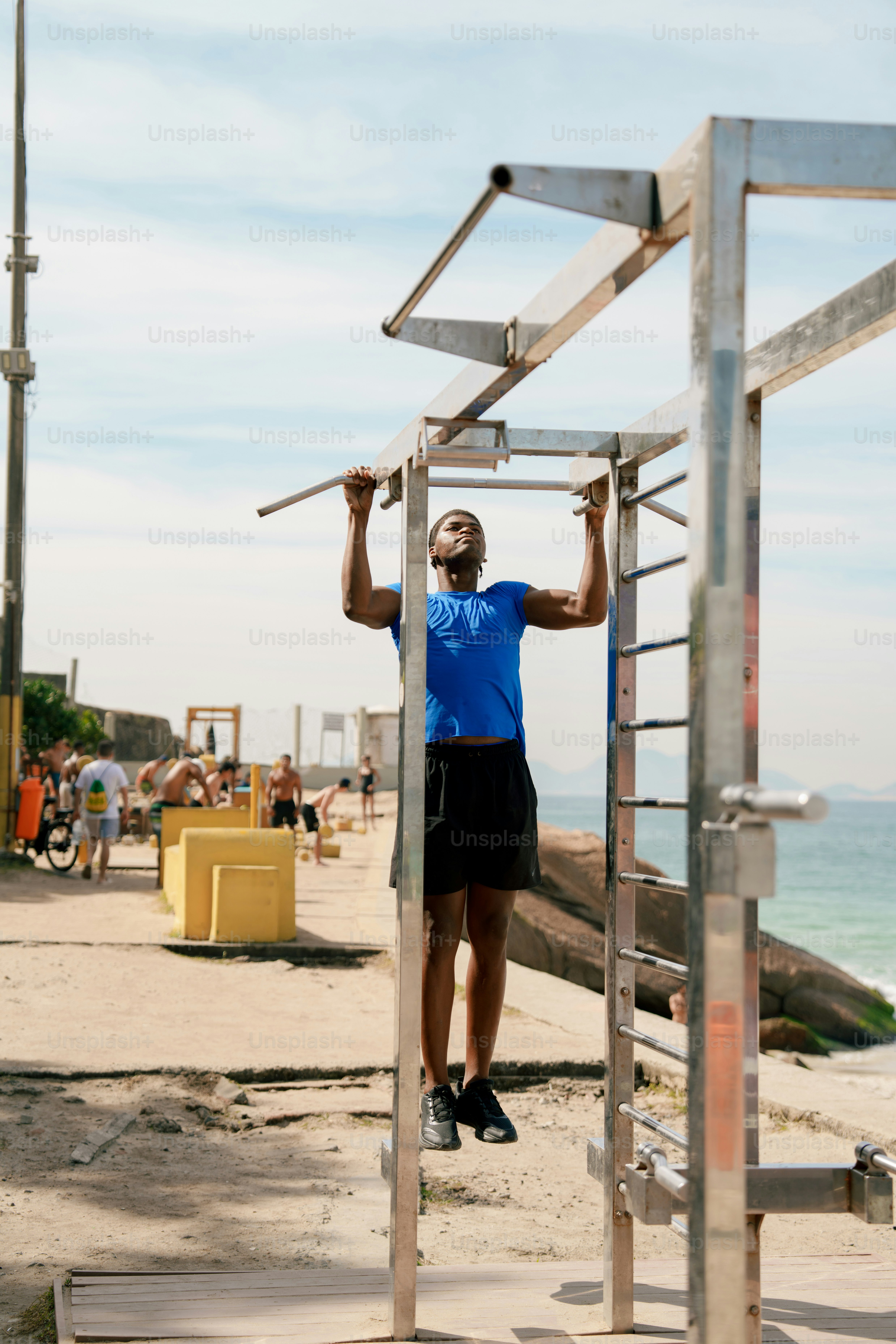 Man performing pull-ups on outdoor gym equipment by the sea.