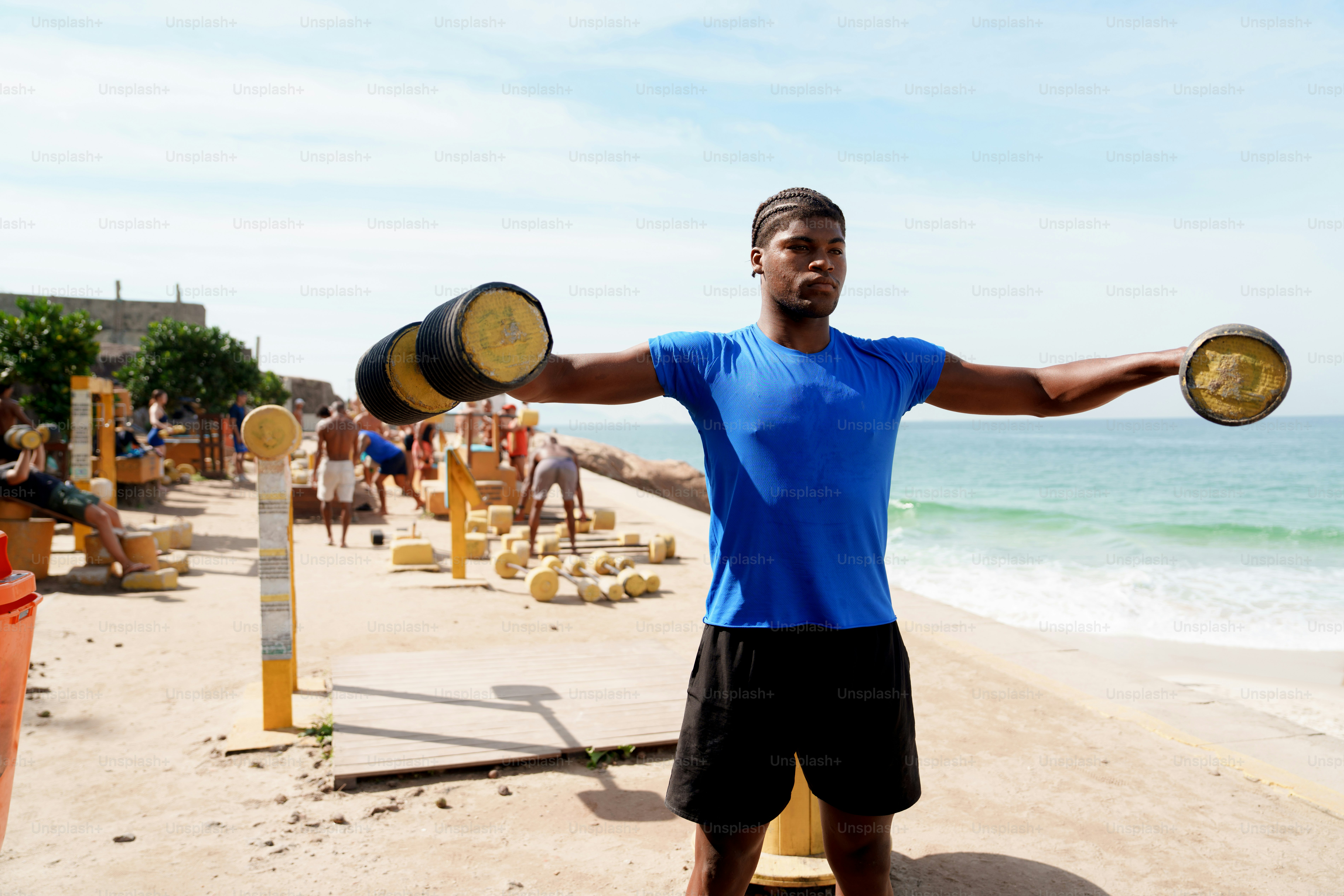 Man exercising with weights on a sandy beach.