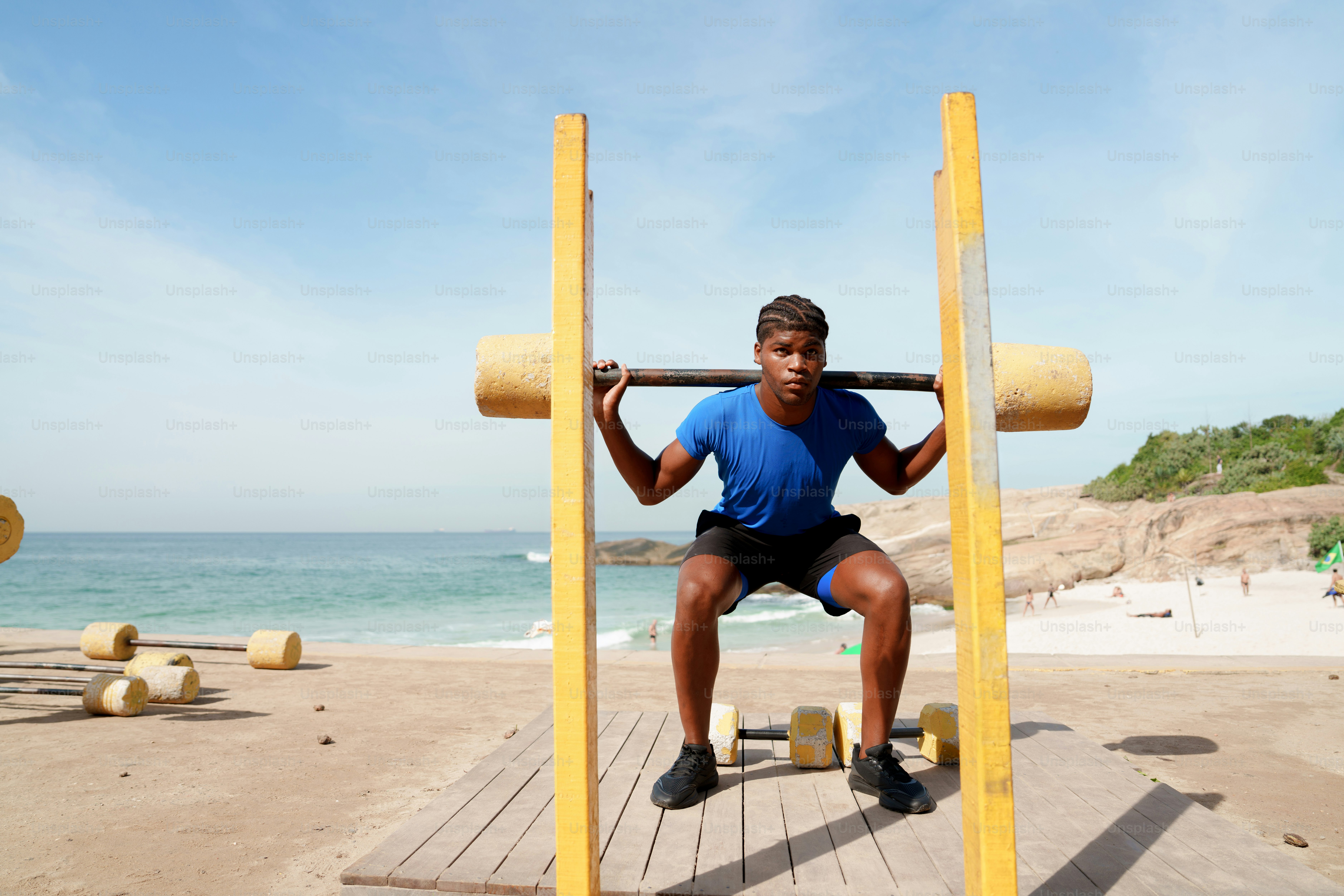 A man squats with a bar on a beach.