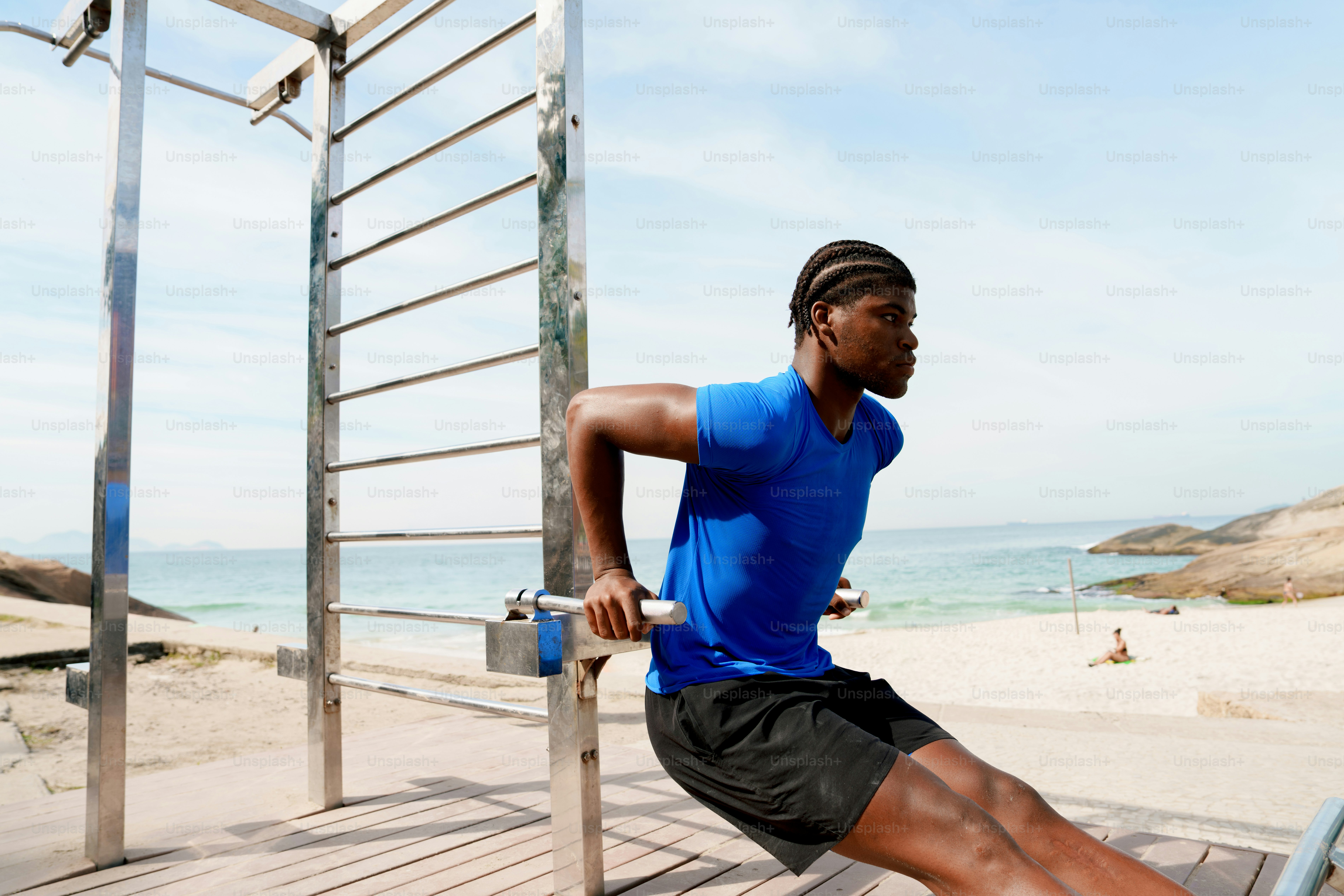 A man doing dips on outdoor equipment near the beach.