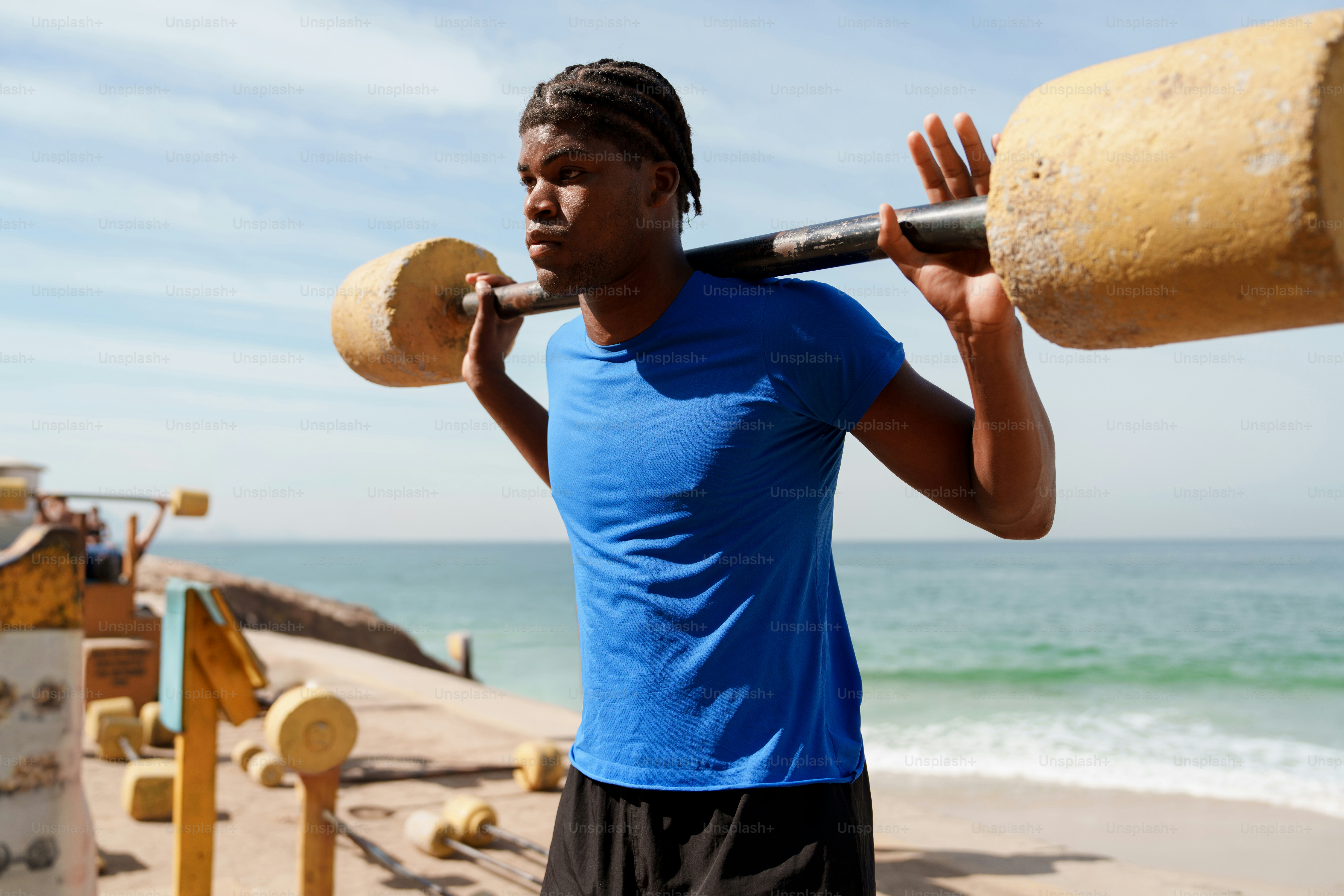 Young man lifting a unique barbell by the ocean.