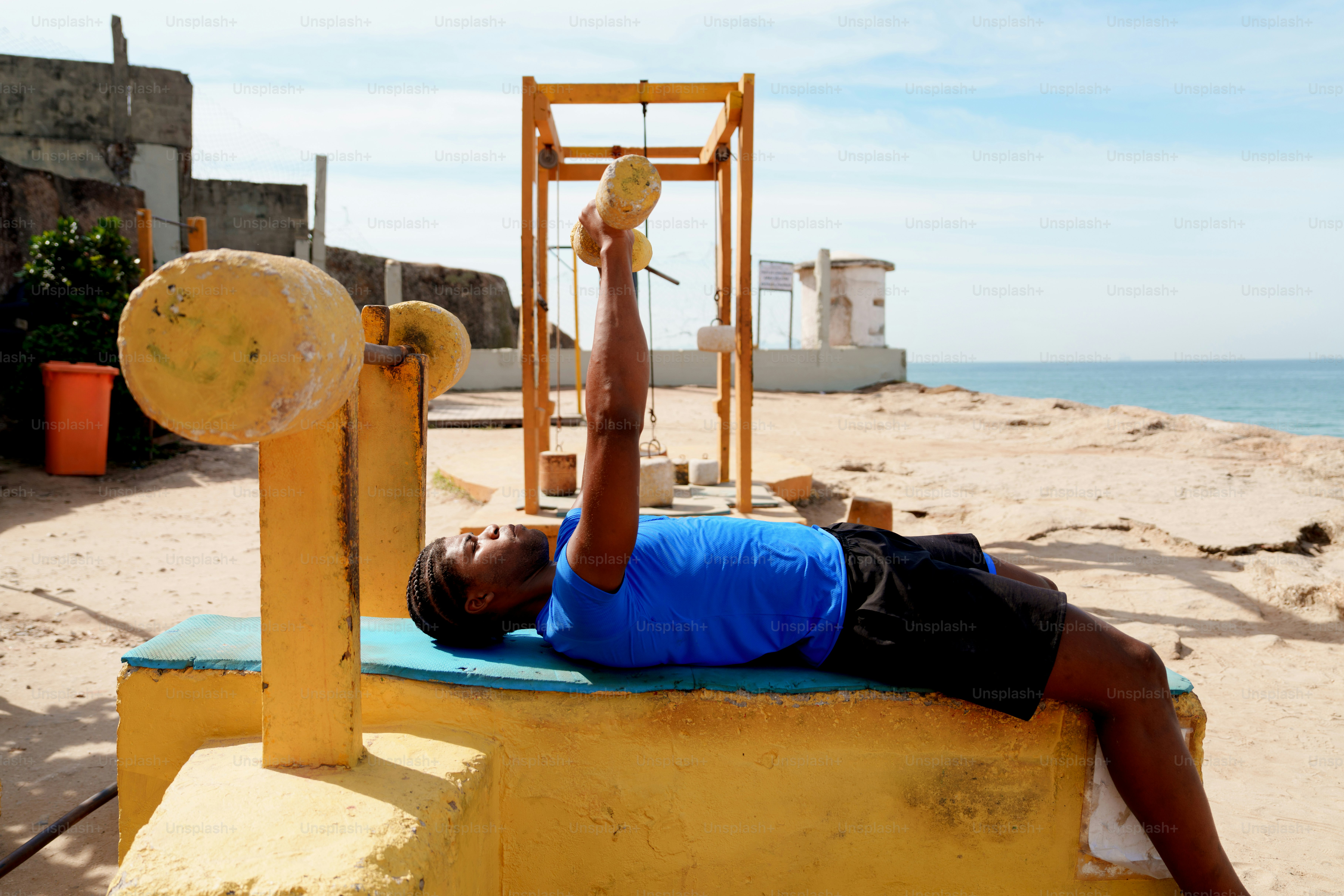 A man lifts homemade weights on a beach gym.