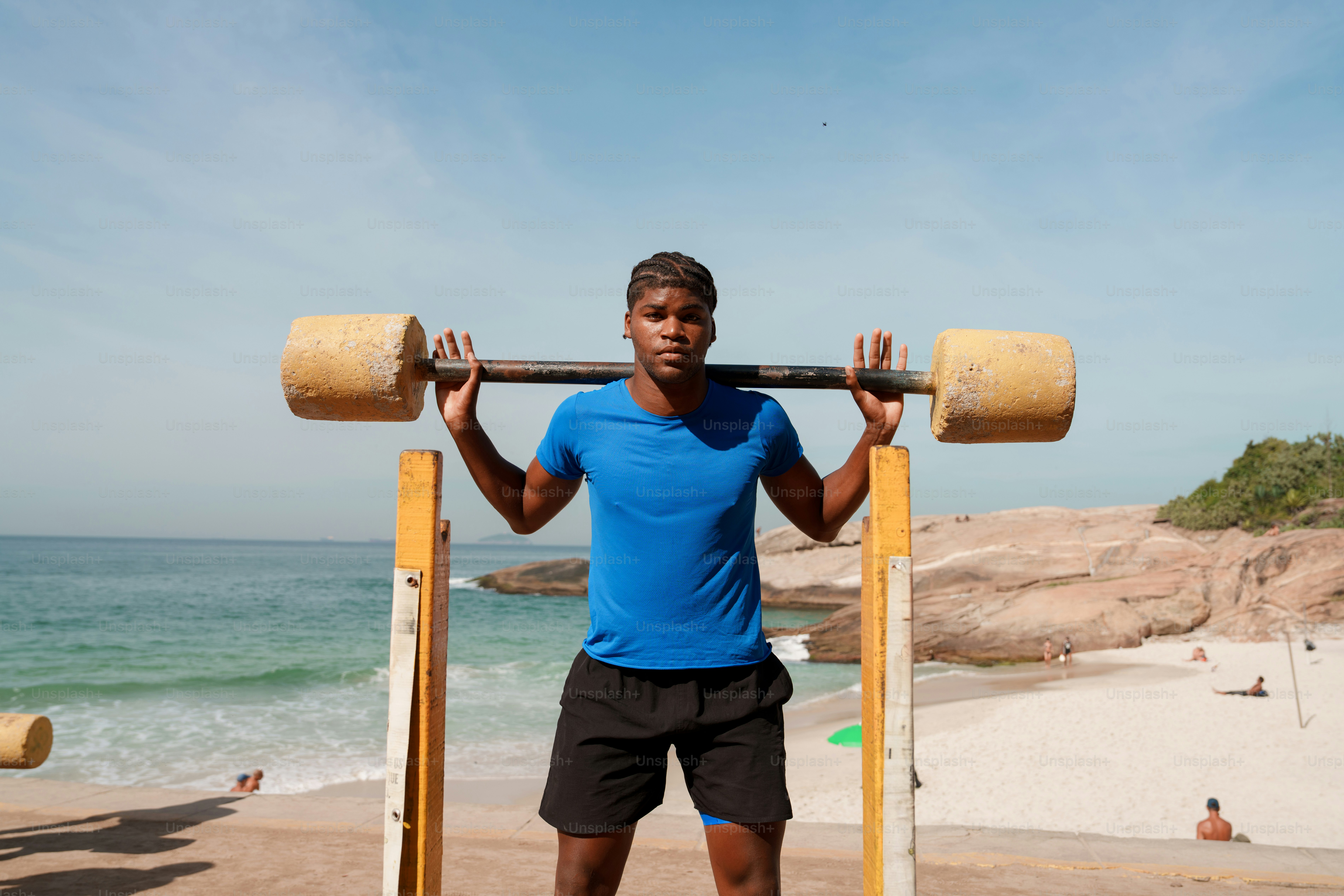 A man lifts a barbell on a sunny beach.