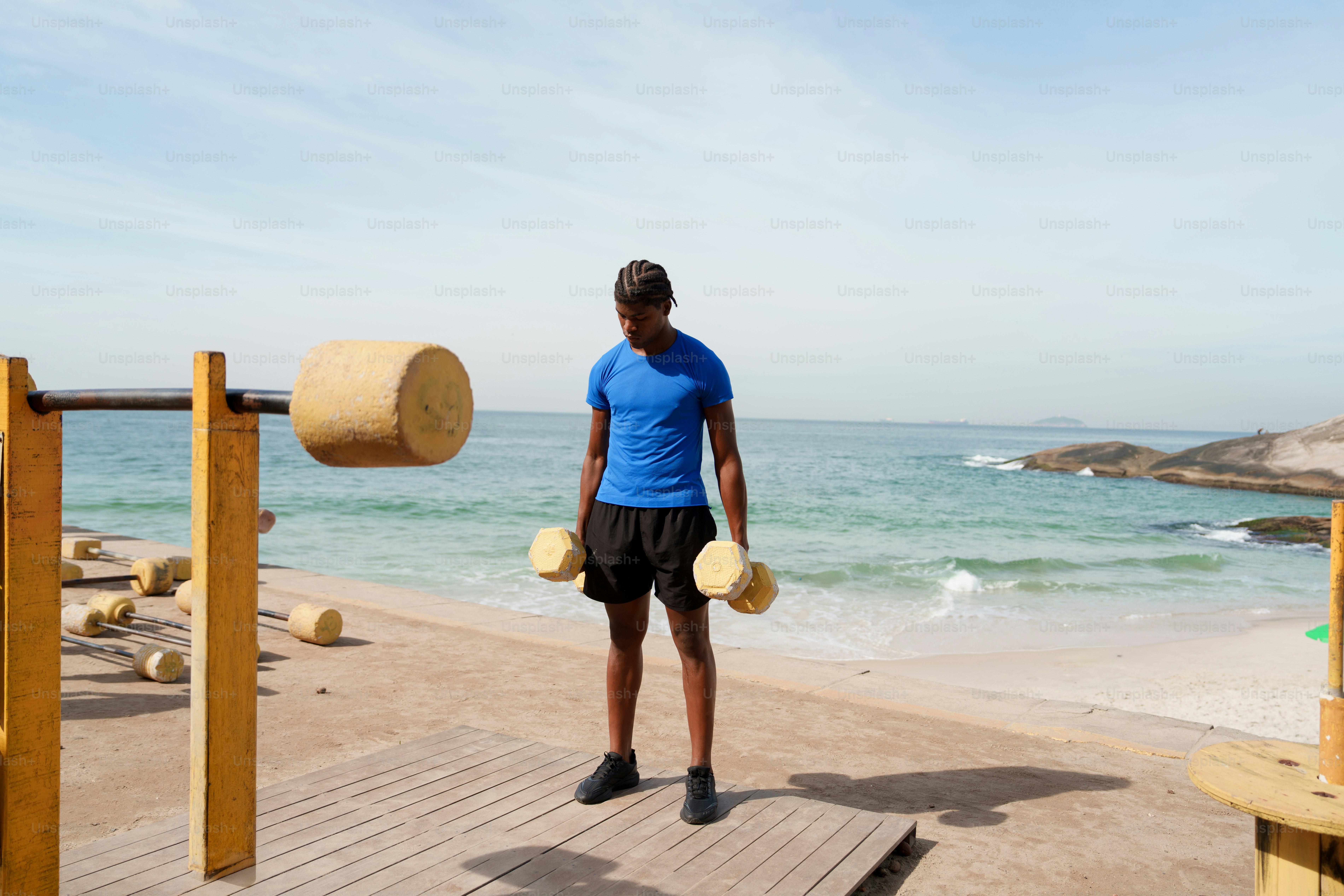 Man holding dumbbells at an outdoor beach gym.