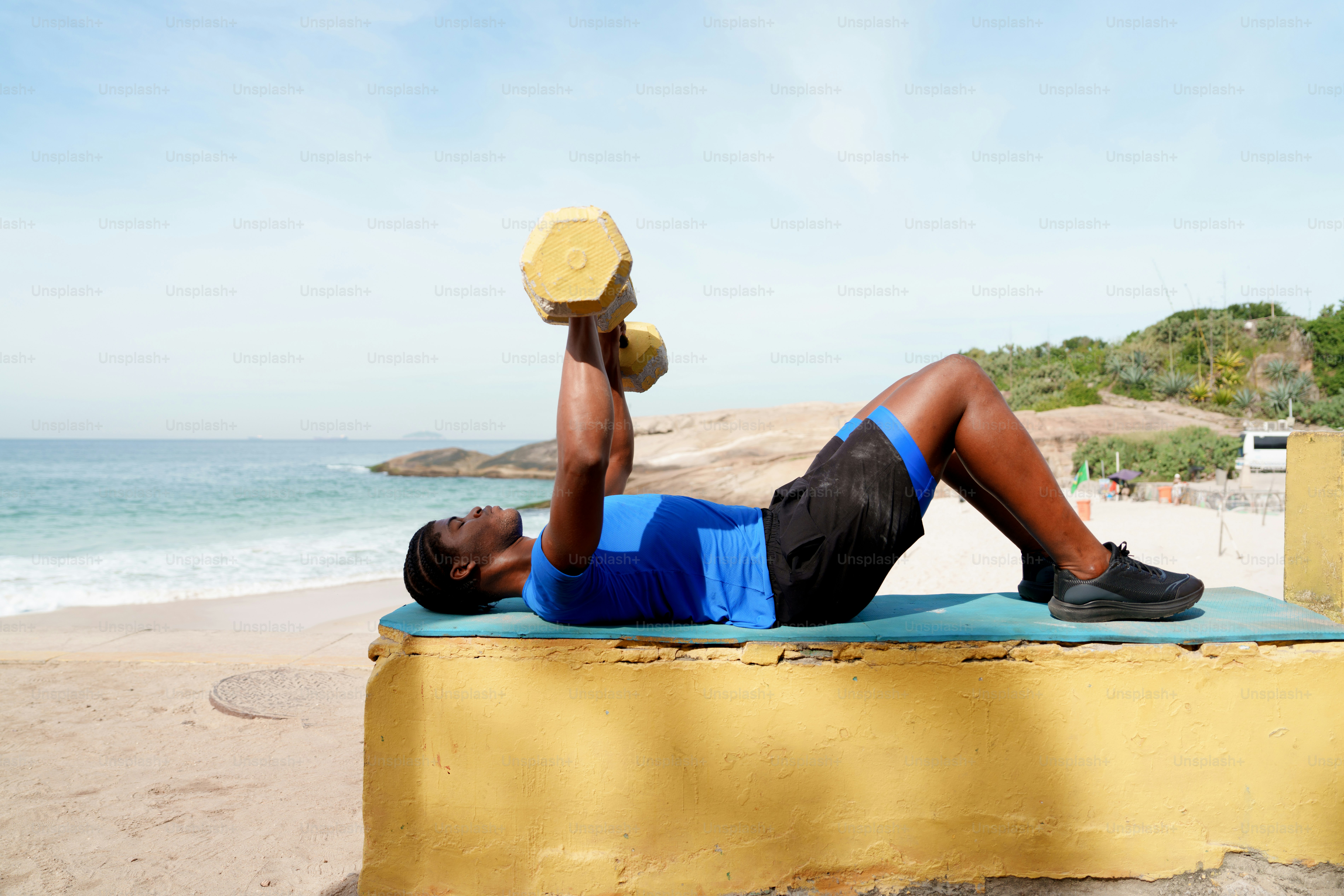 Athletic man exercising with a dumbbell by the ocean.