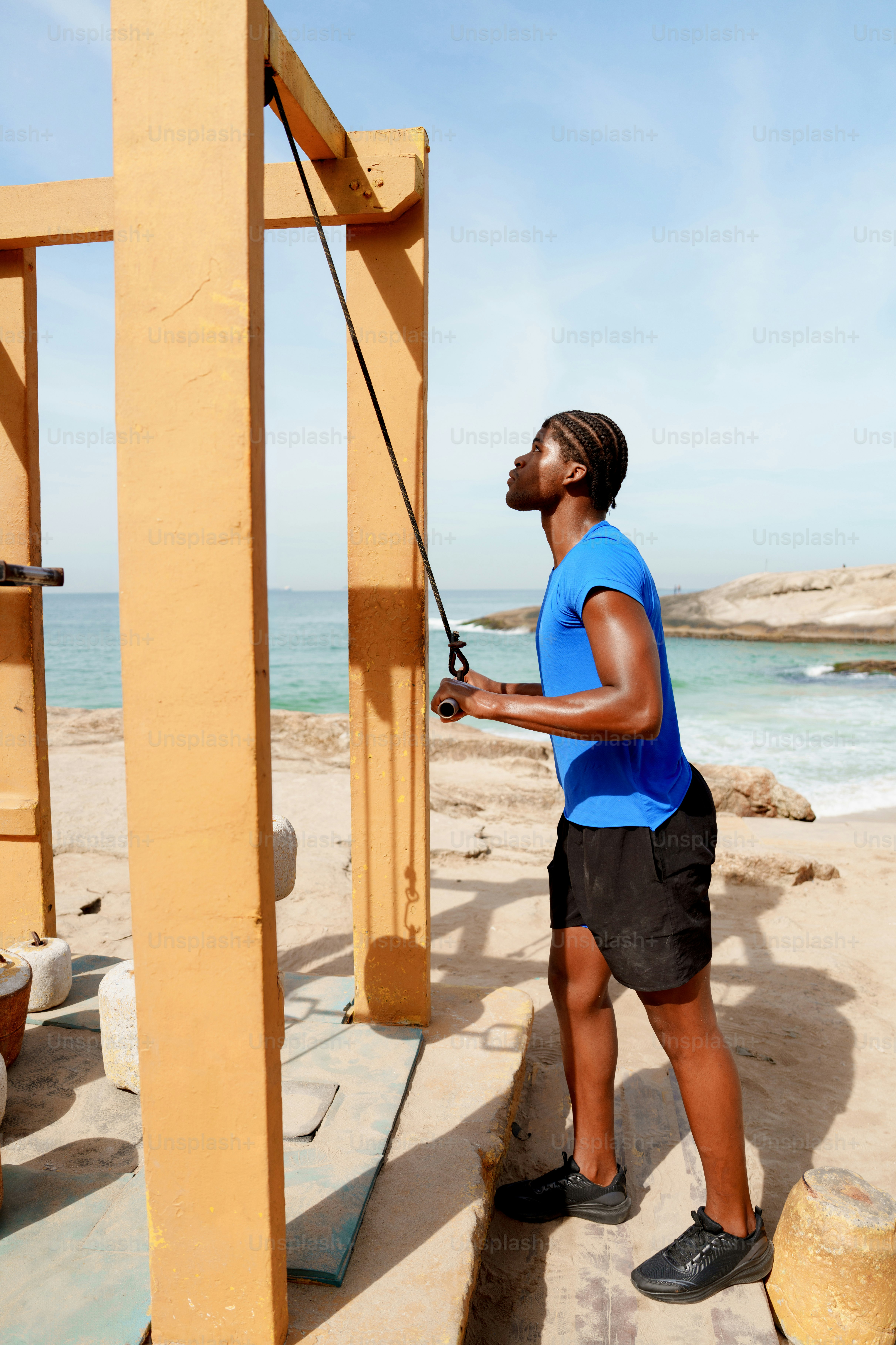 Athletic man uses outdoor gym equipment by the ocean.