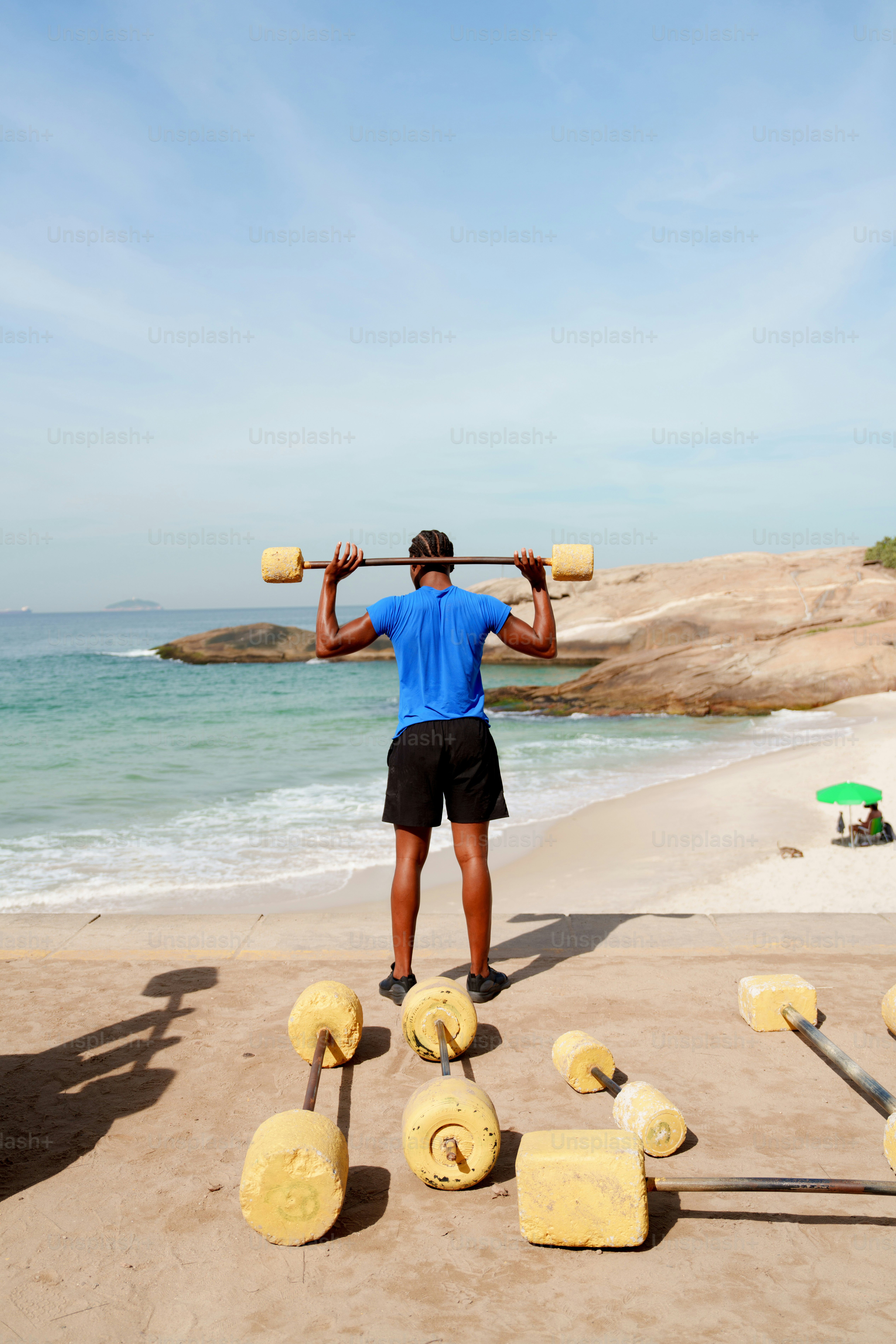 Man lifting weights on a sunny beach by the ocean.