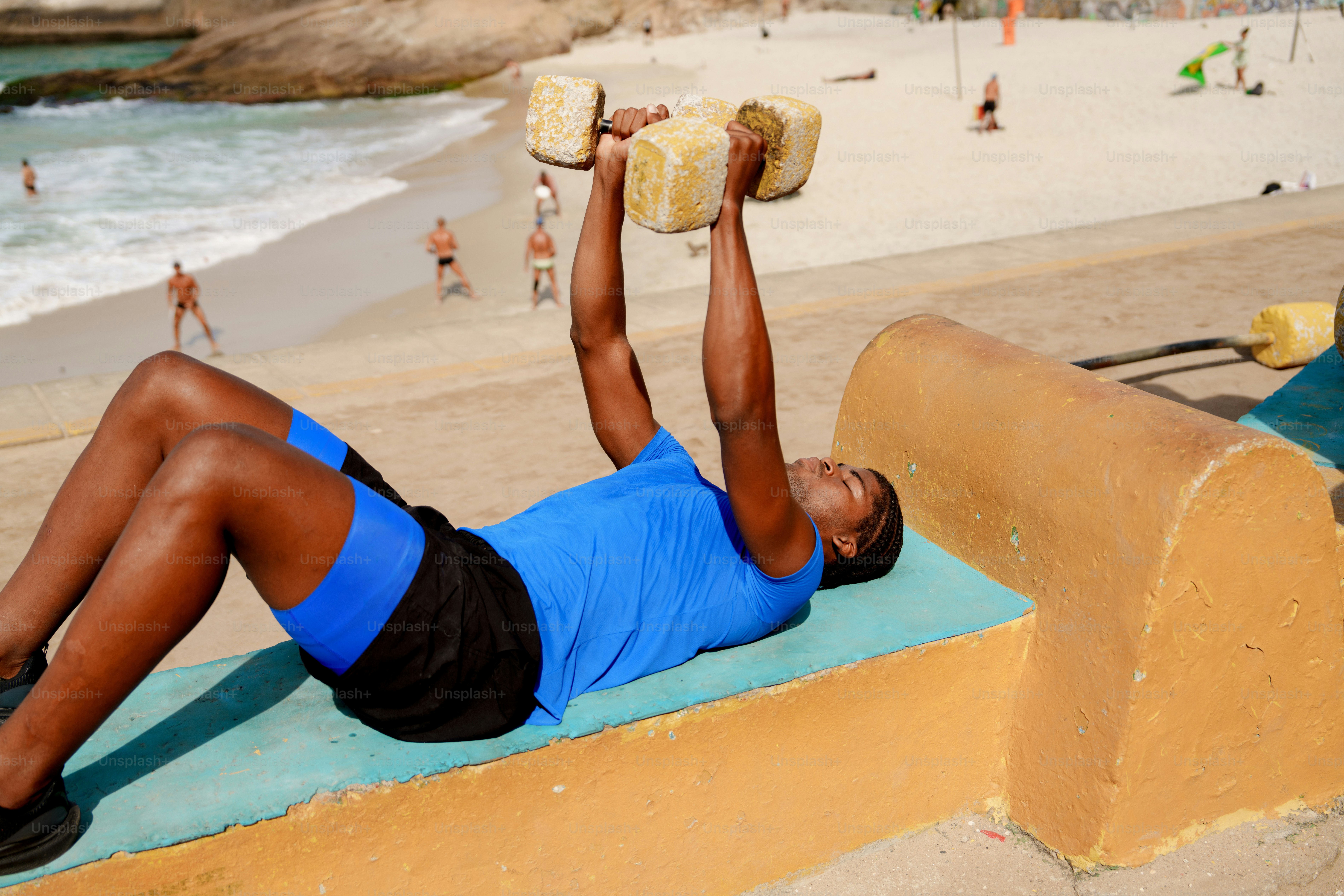 A man exercising with dumbbells on a beach promenade.