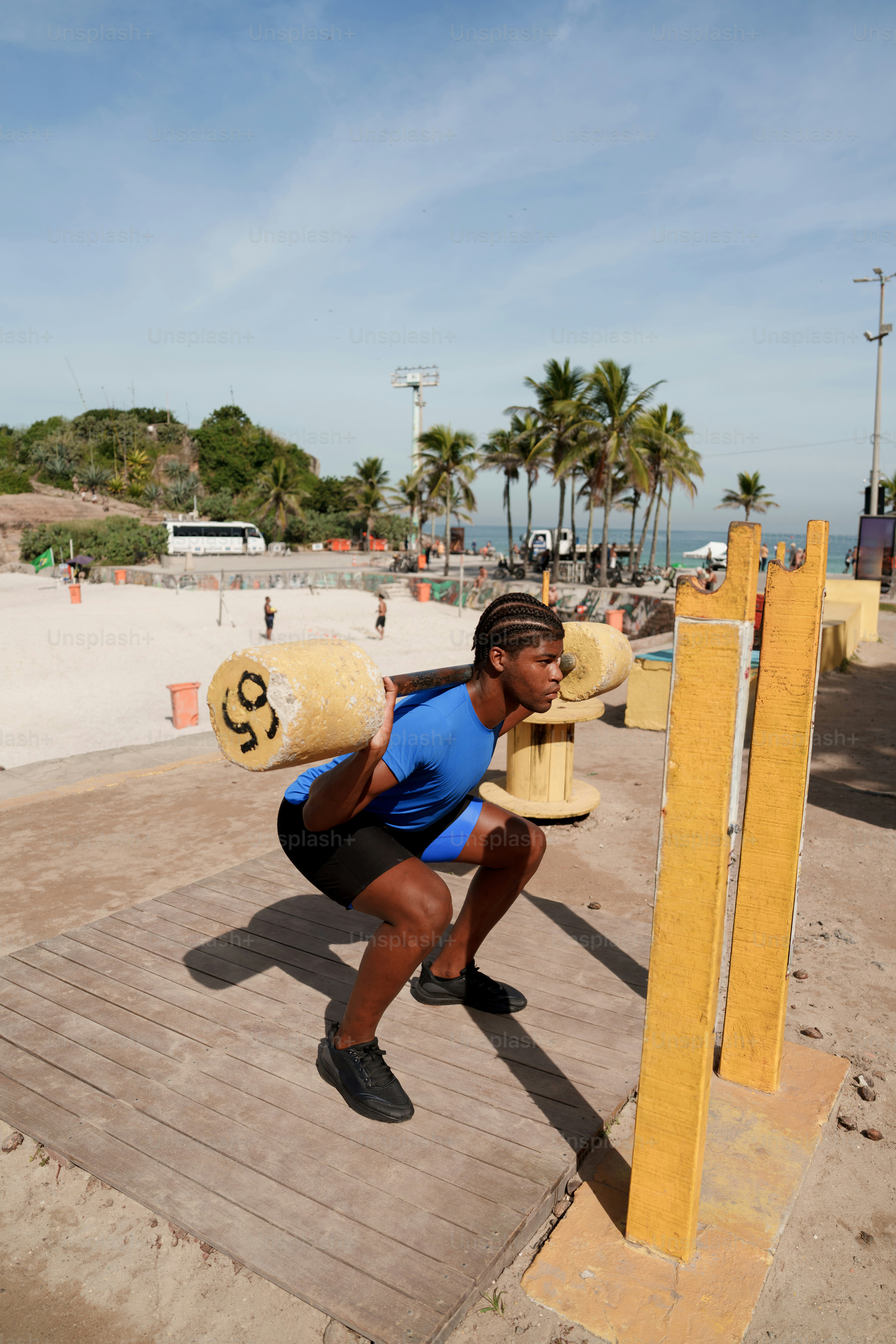 Athlete squats with a log barbell on a sunny beach.