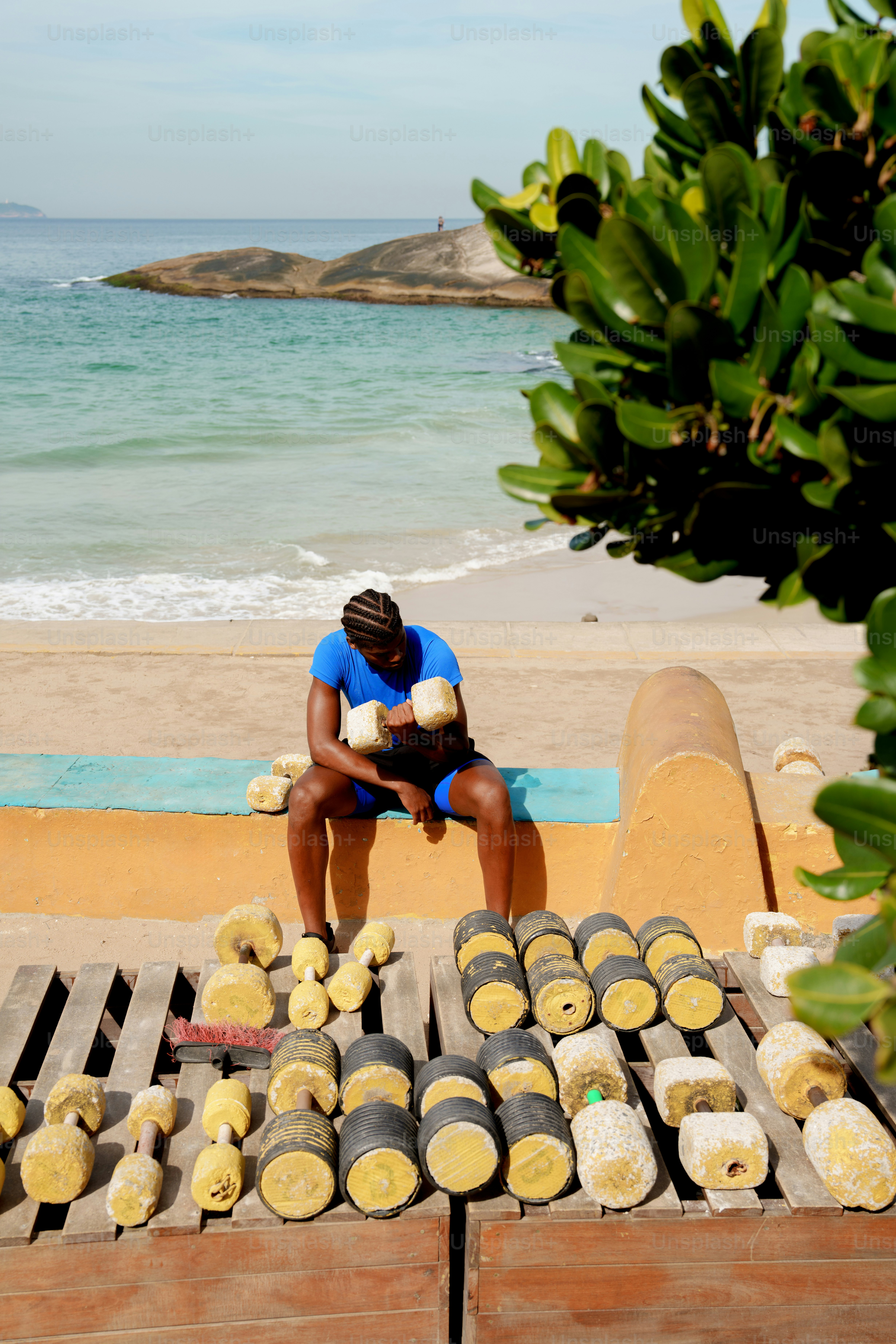 A person exercises with handmade dumbbells on a sunny beach.