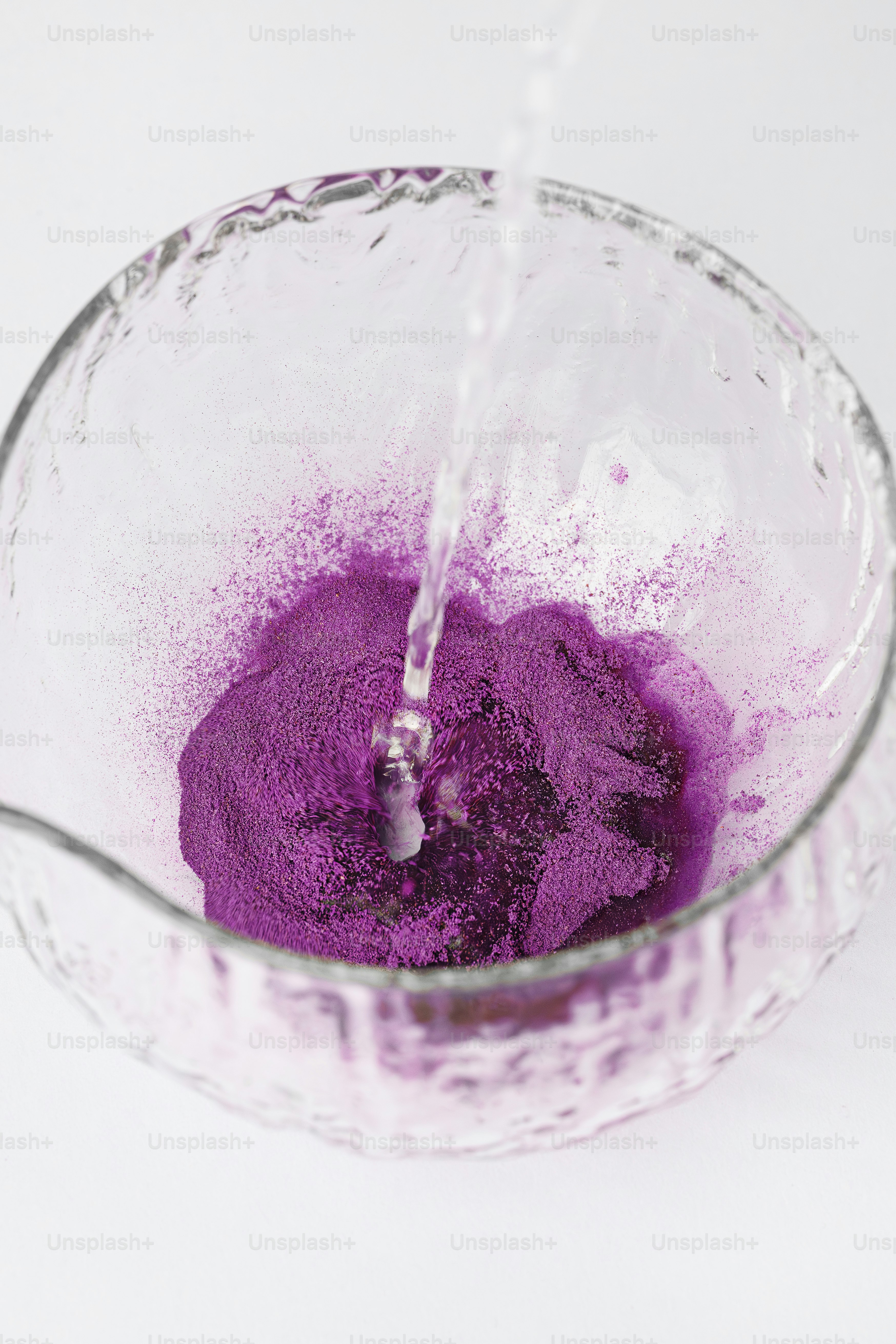 Water pours into a glass bowl with purple powder.
