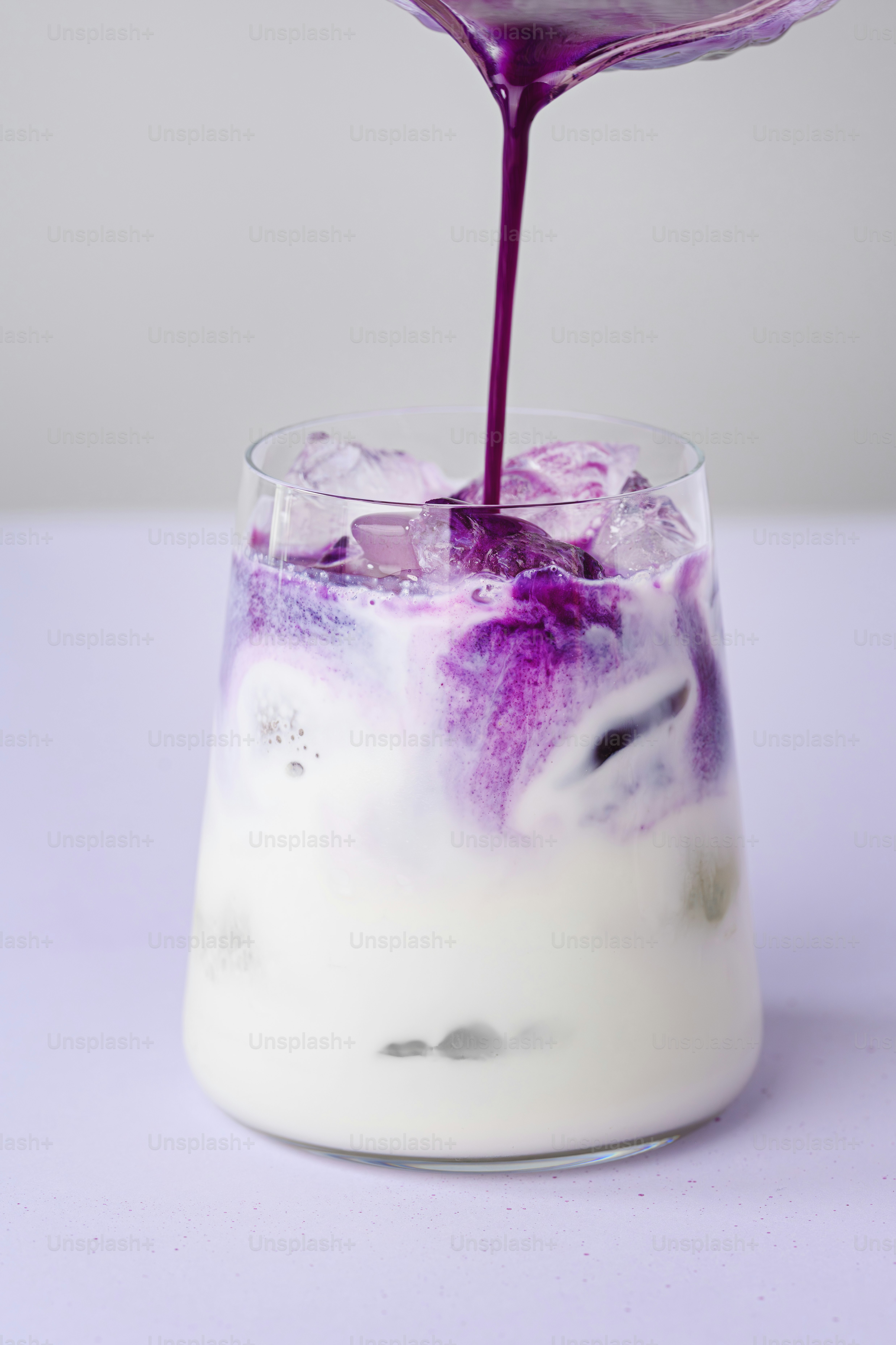 Purple liquid pours into a glass of iced milk.