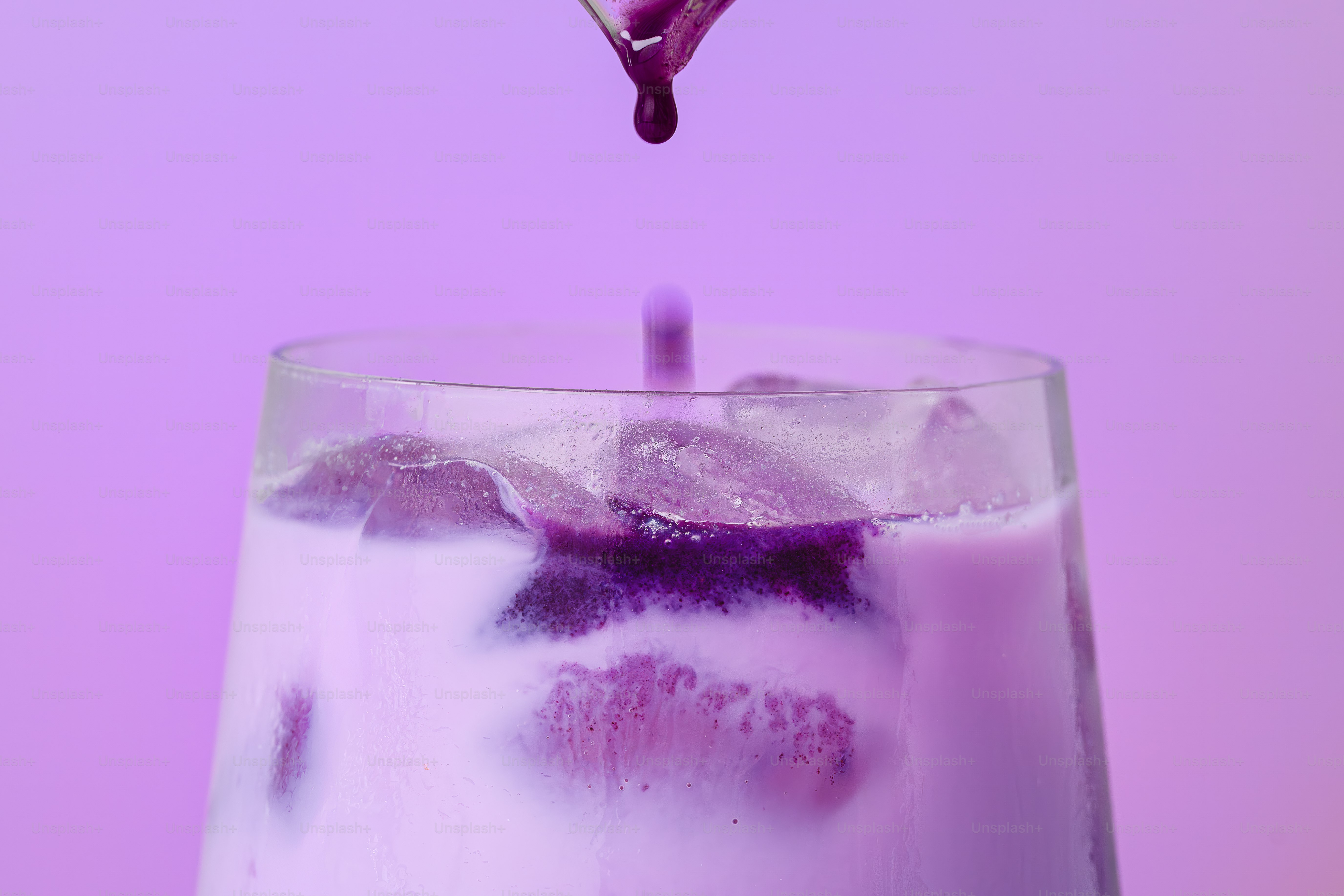 Purple liquid drips into a glass of milky purple drink.