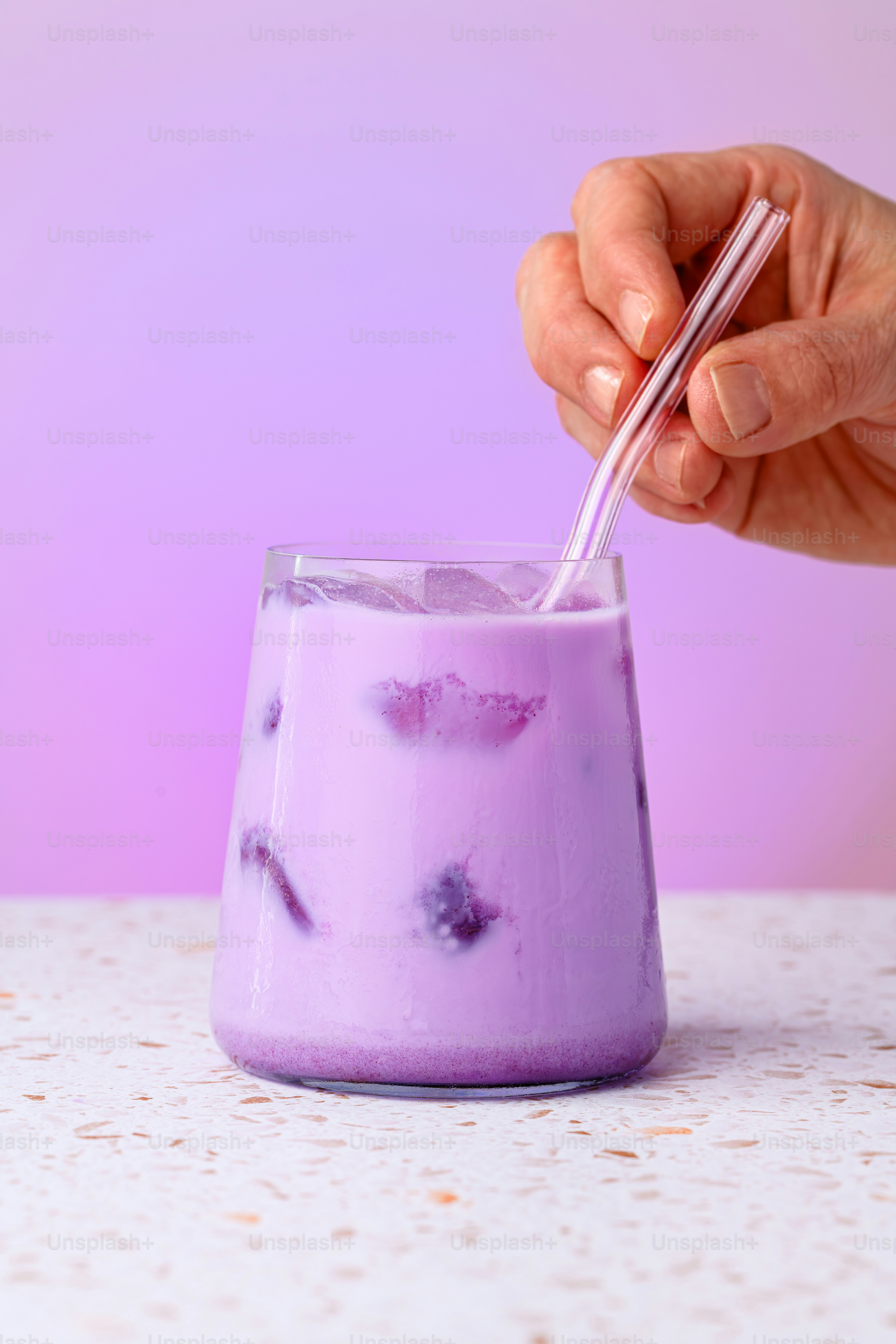 Hand stirring a purple iced drink with a straw.