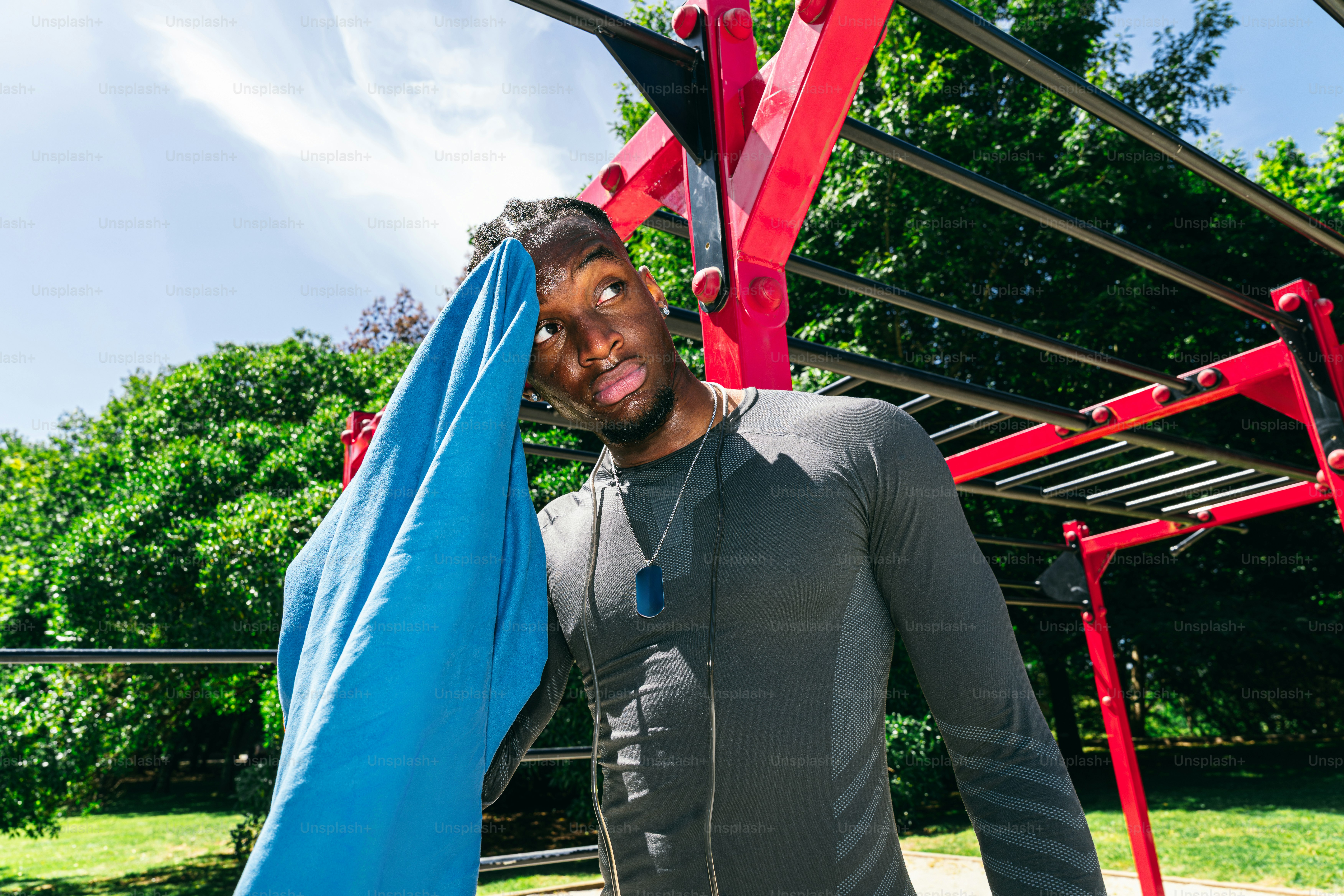 Sweaty man wipes face with blue towel at outdoor gym.