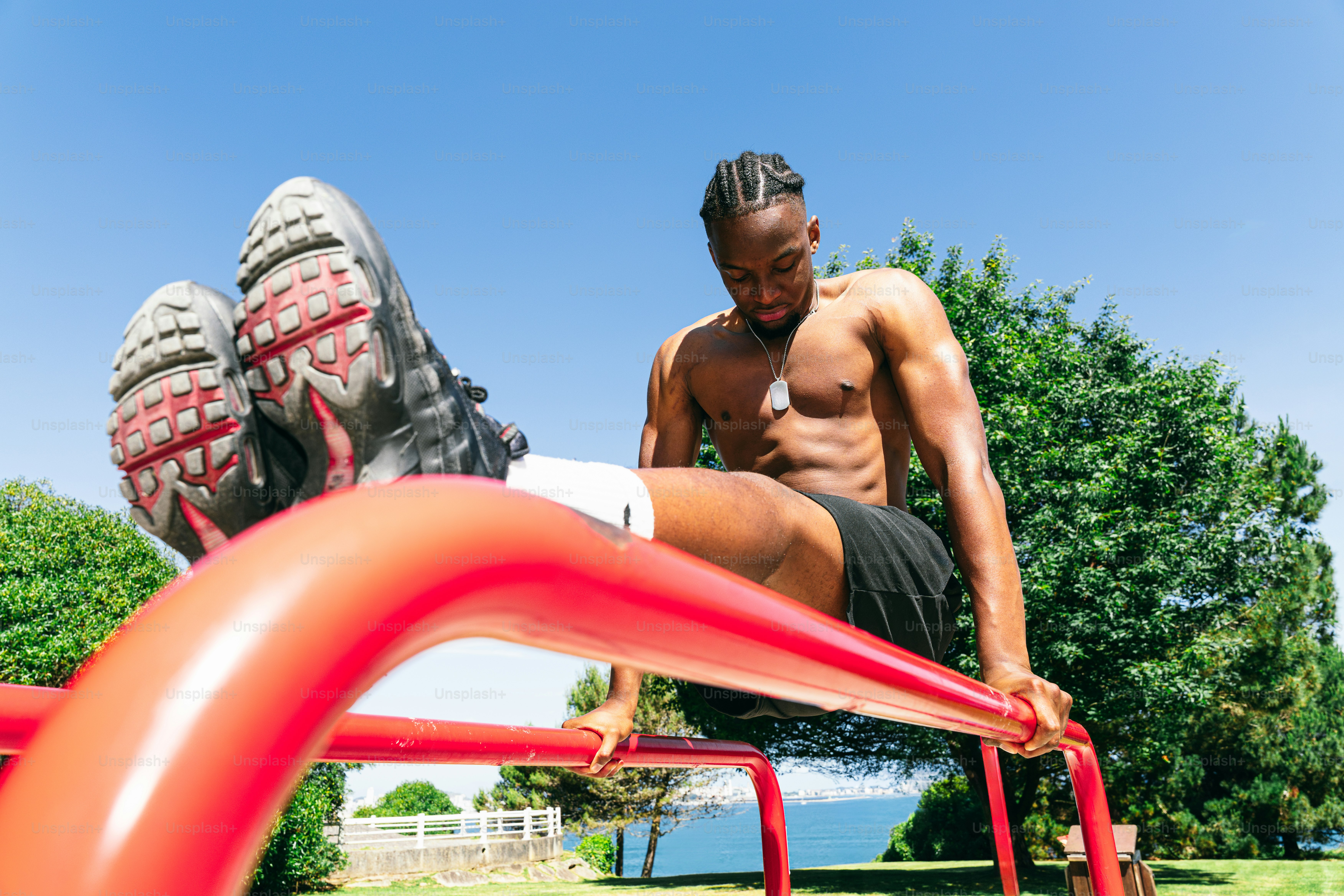Shirtless man exercising on red parallel bars outdoors.