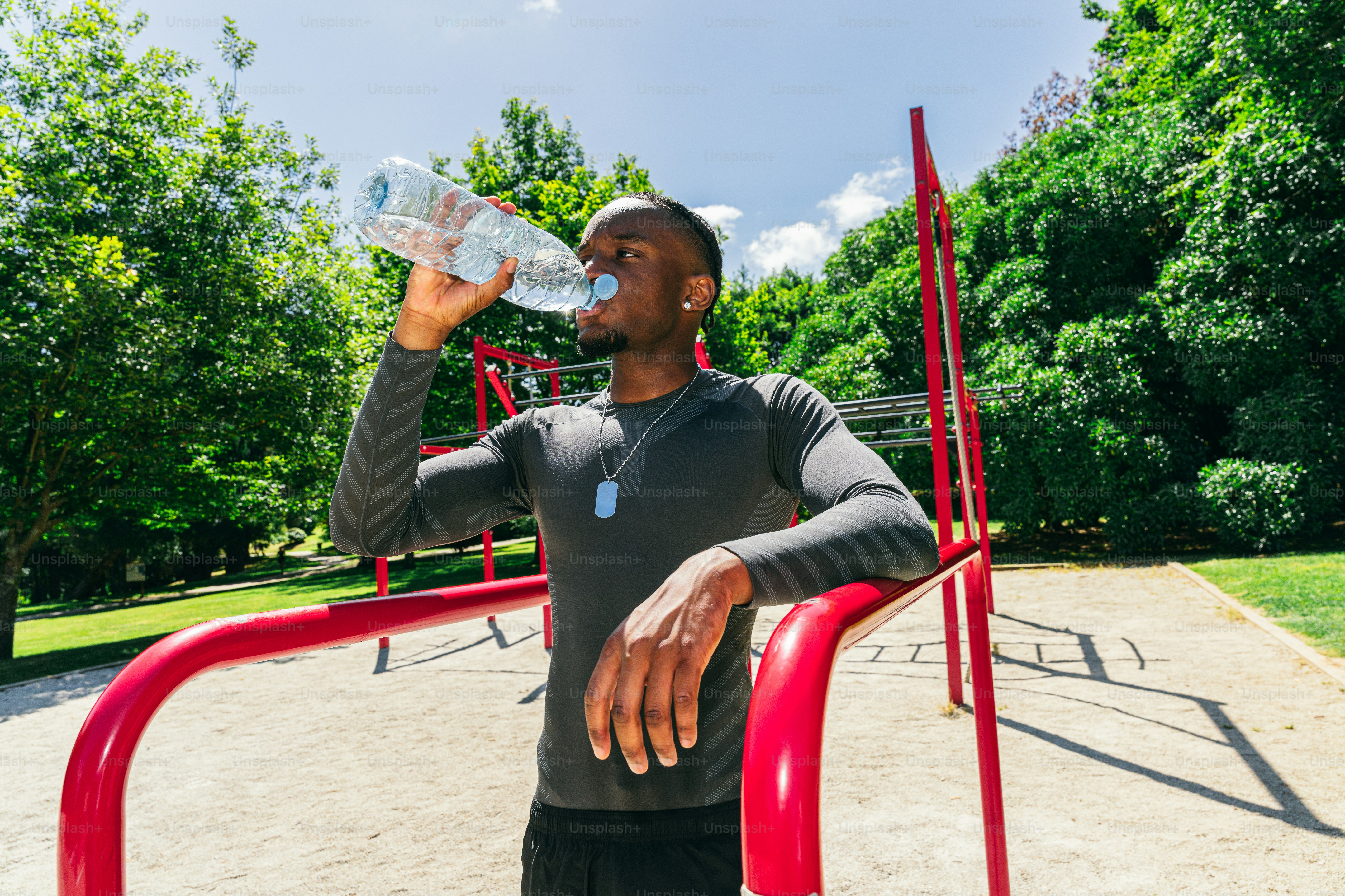 Man drinking water in a sunny outdoor gym.