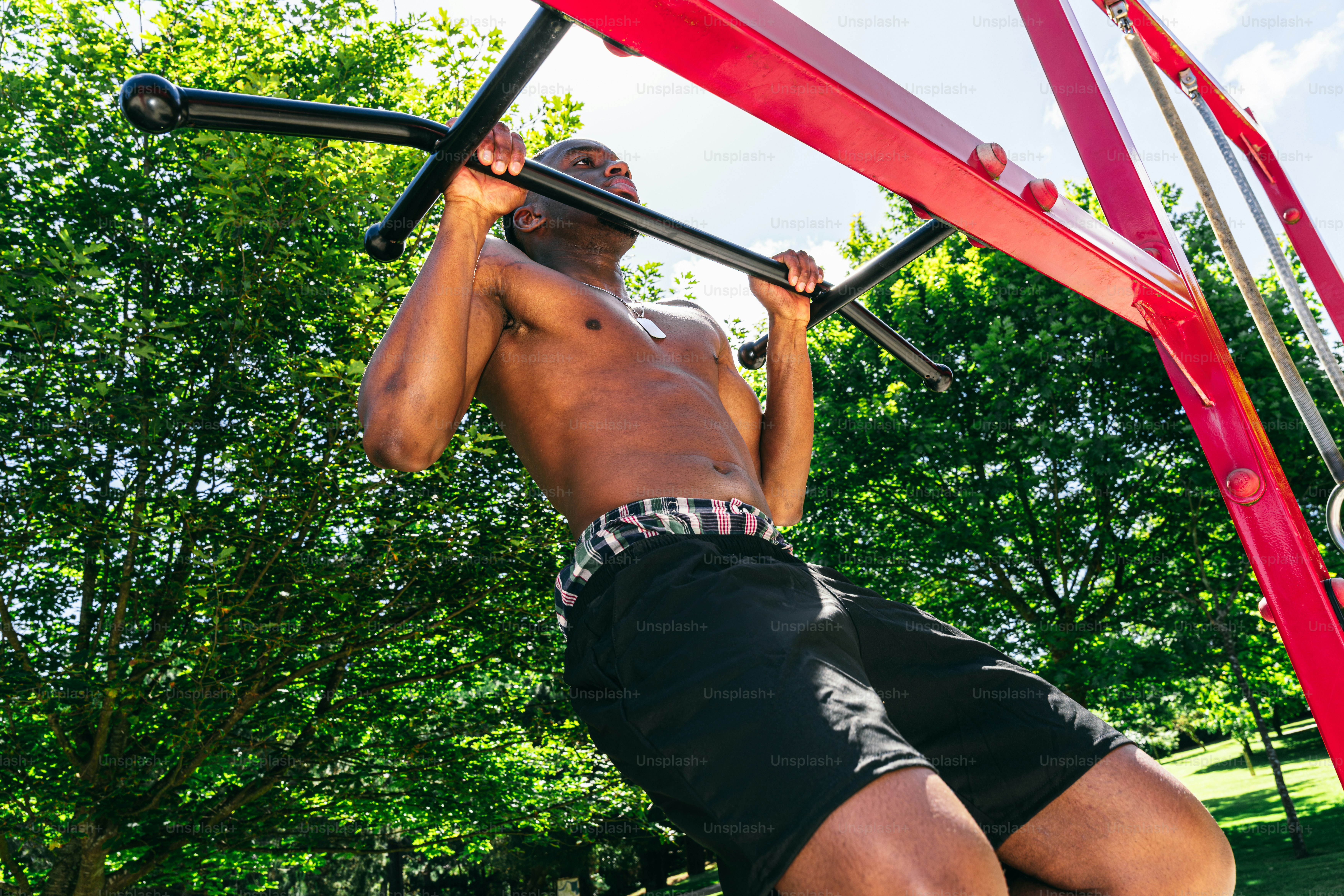 A shirtless man doing pull-ups on an outdoor exercise frame.
