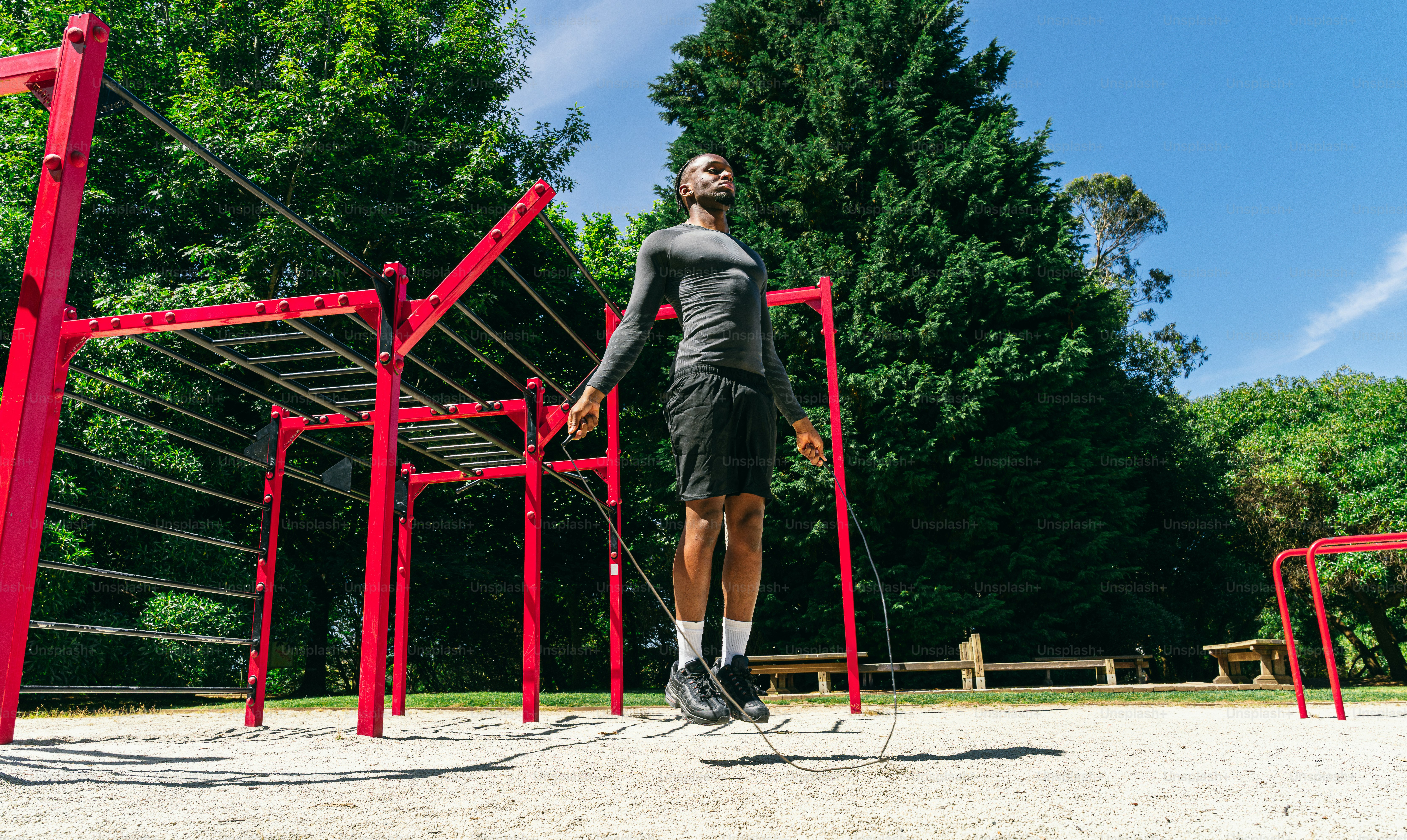 A man jump roping outdoors near red exercise equipment.