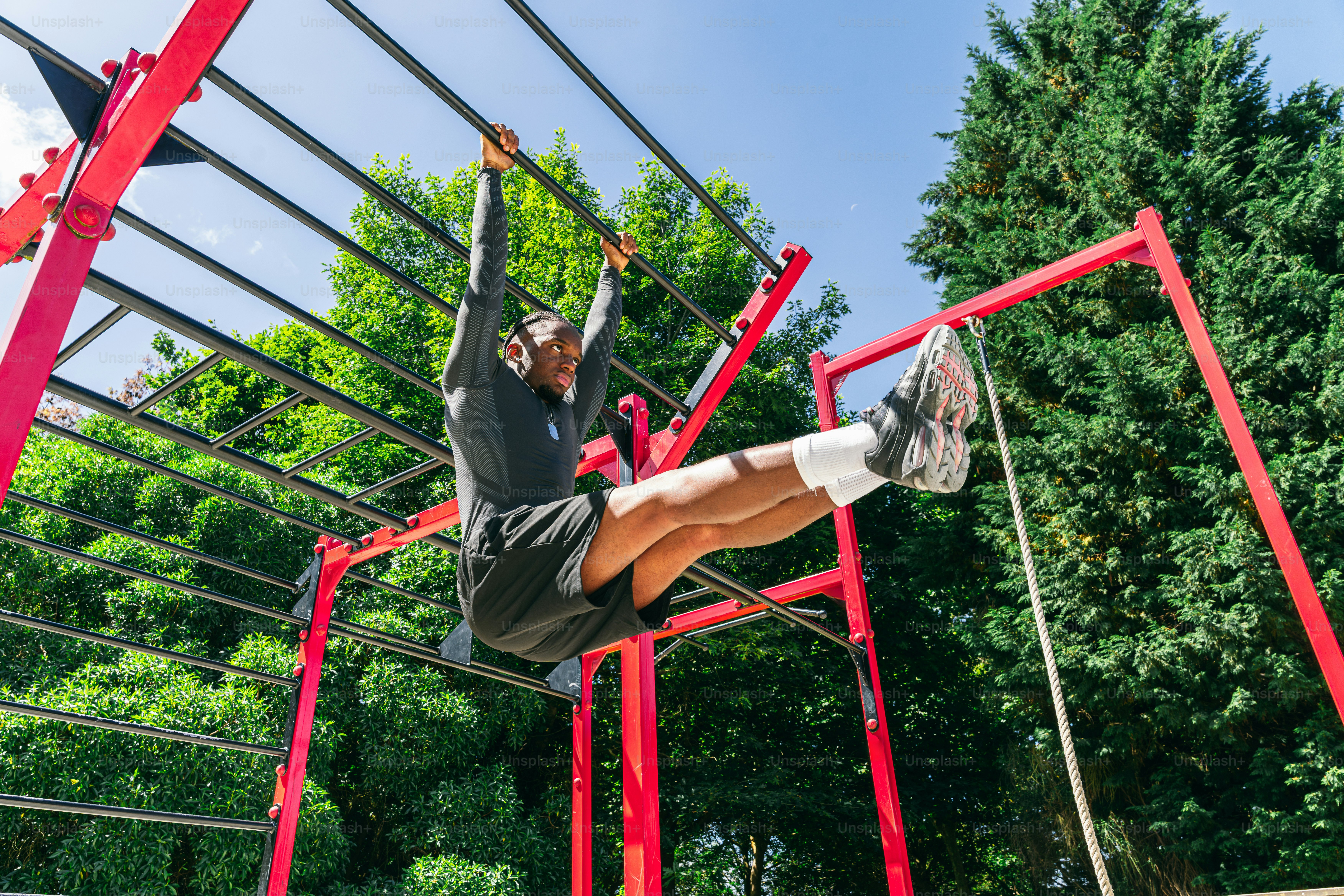 Athlete performing l-sit exercise on outdoor monkey bars.