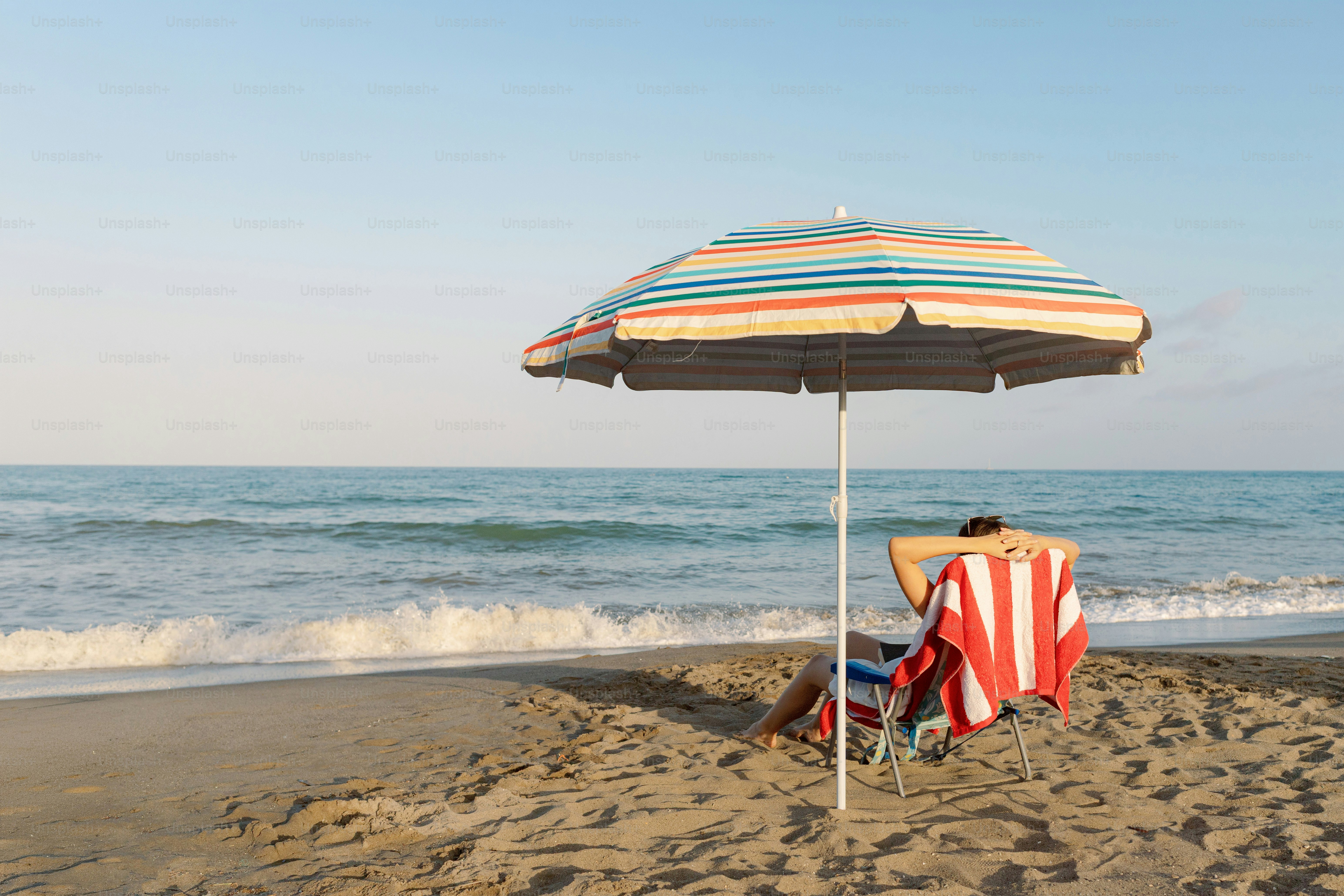 Person relaxing on beach chair under umbrella by the ocean.