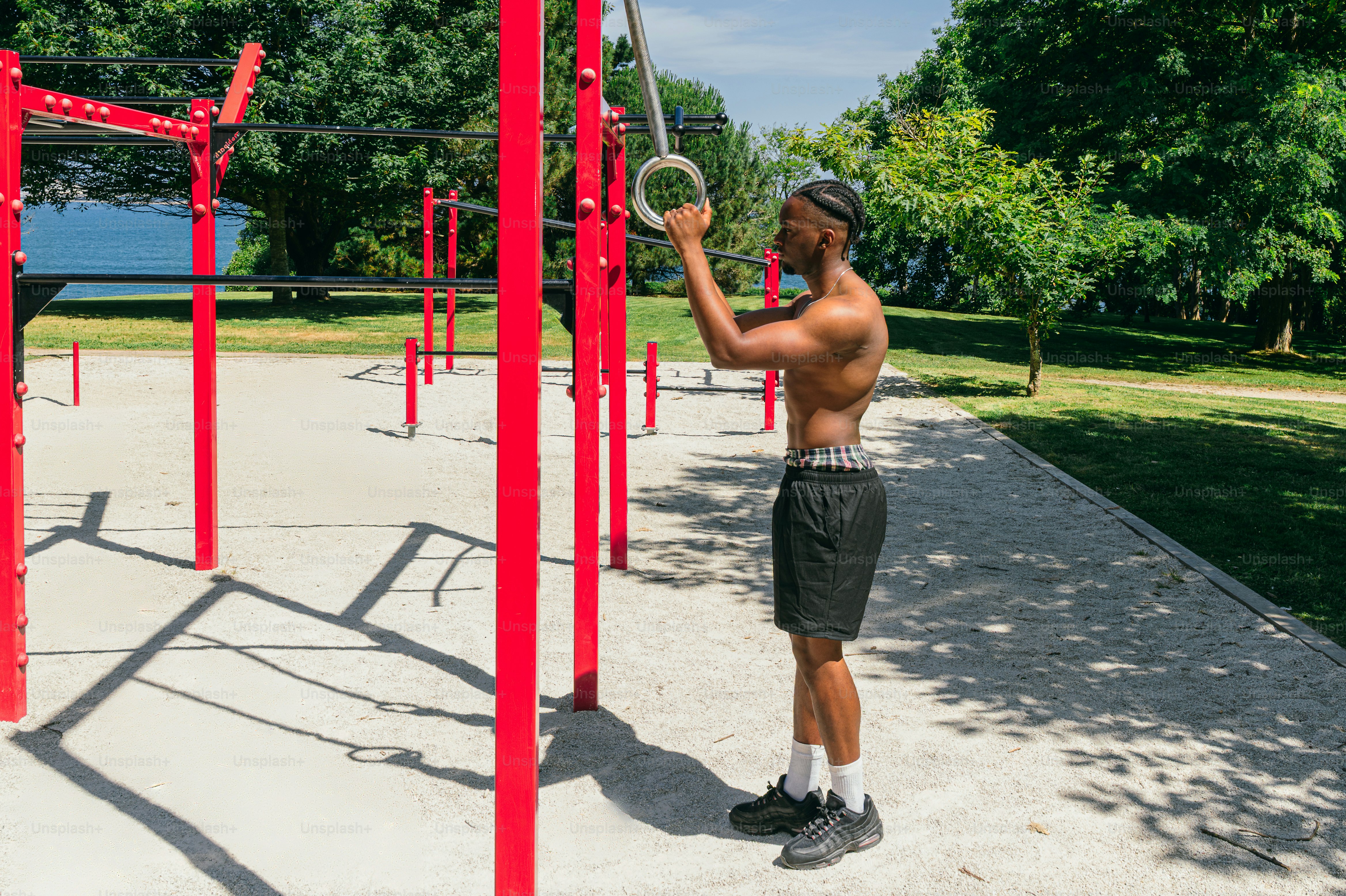 Shirtless man exercising with gymnastic rings in an outdoor park.