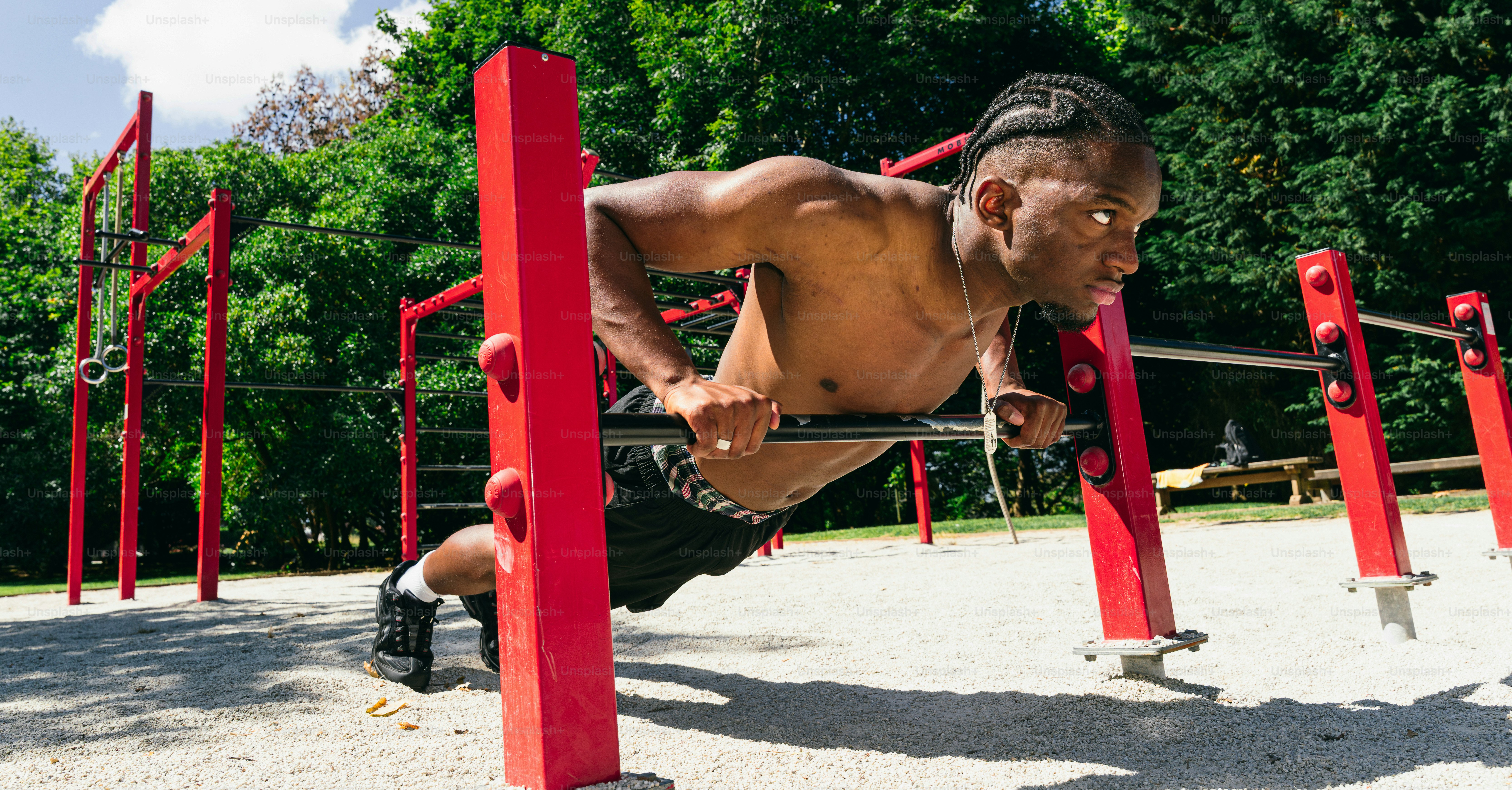 A man doing push-ups on red outdoor exercise bars.
