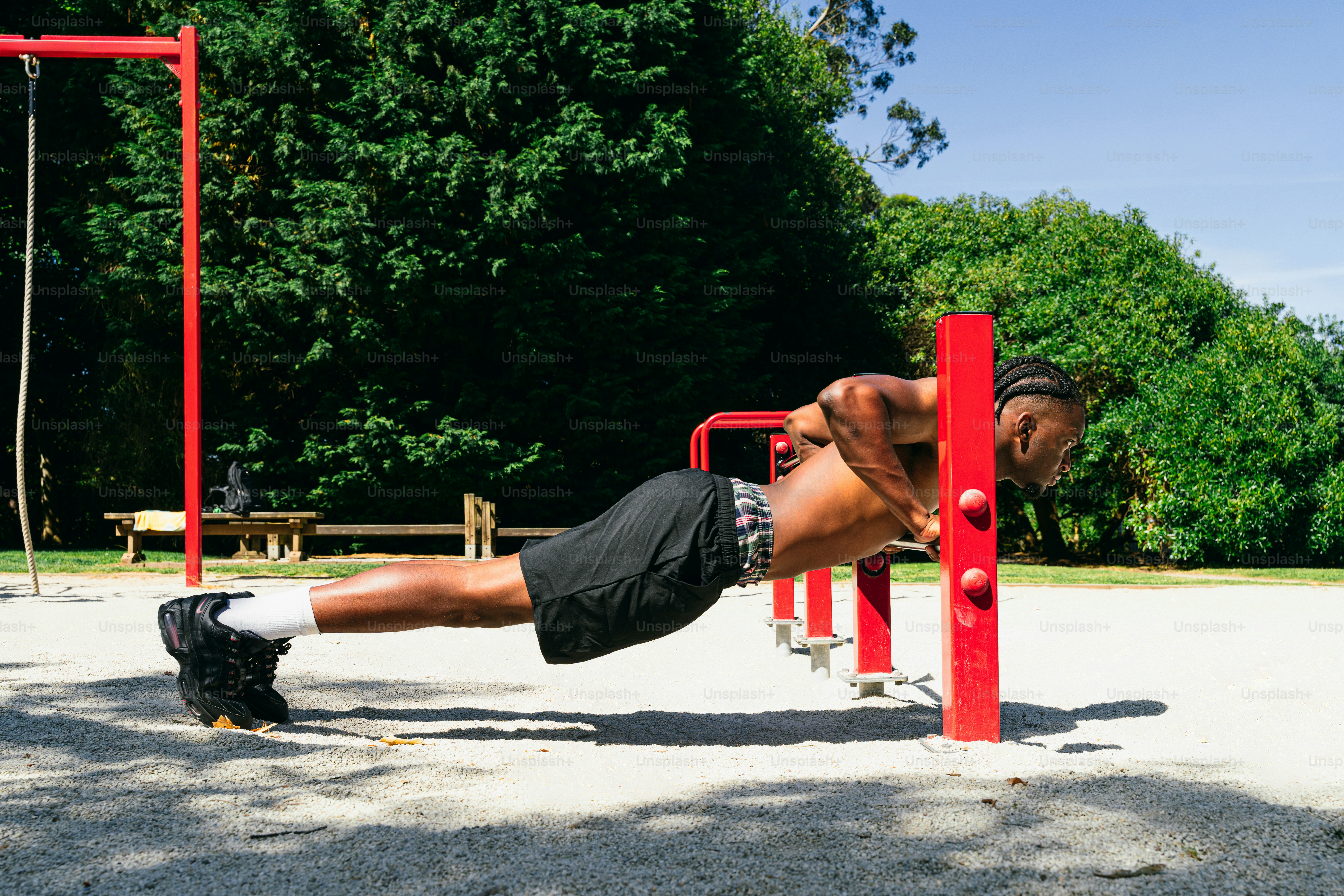 A man doing push-ups on red exercise bars outdoors.