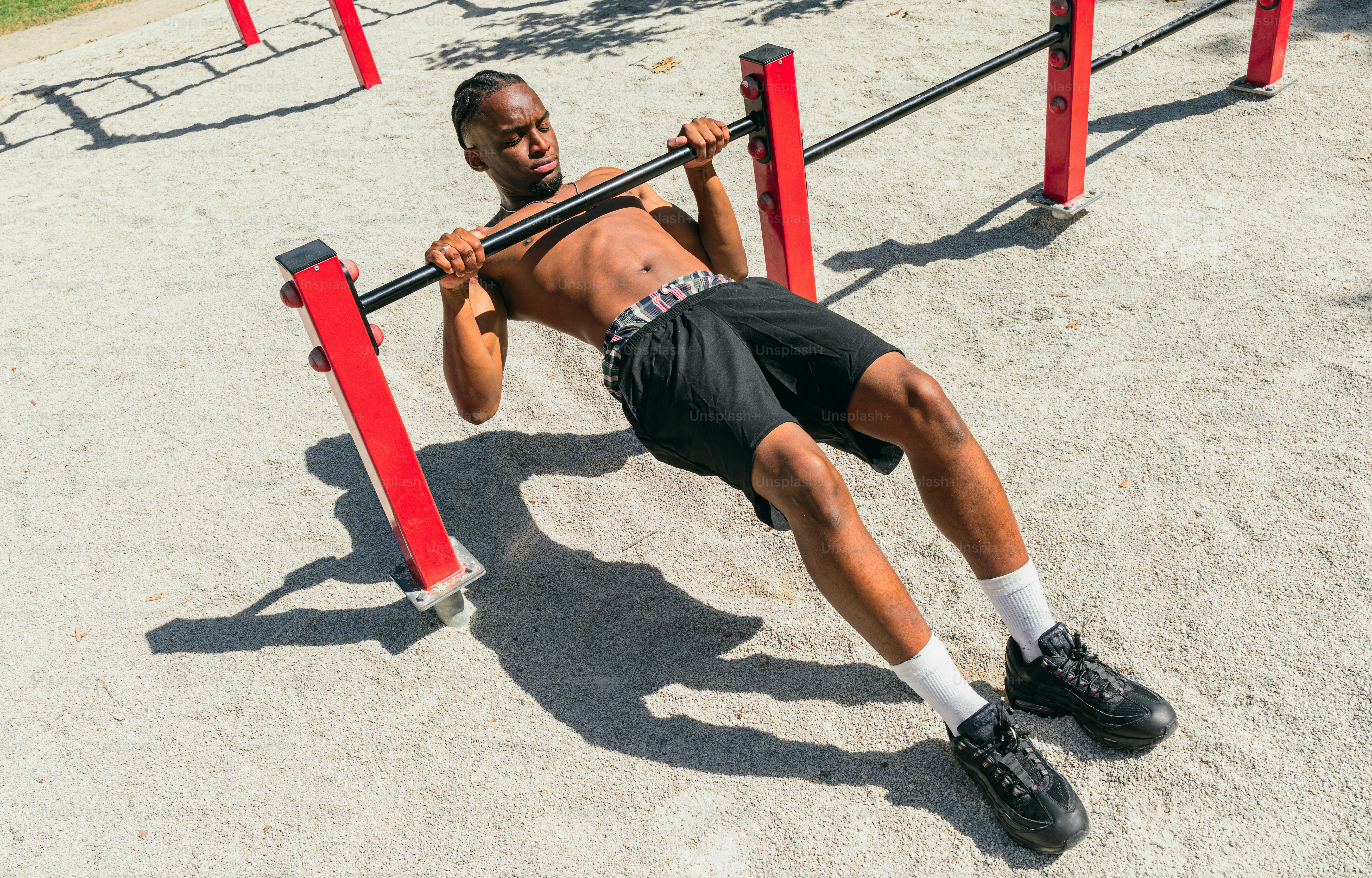 Shirtless man performs inverted rows on an outdoor bar.