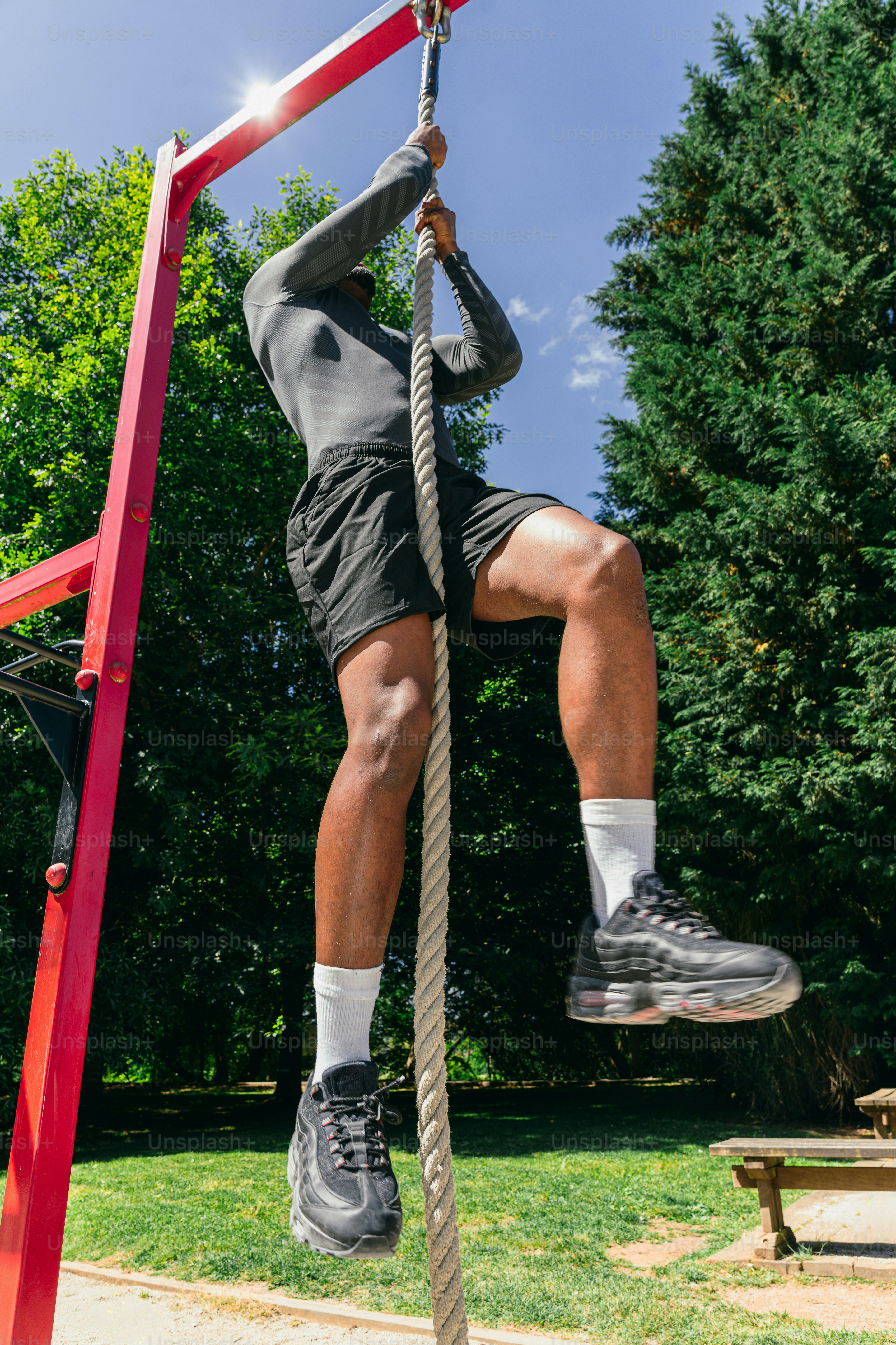 Athletic man climbing a rope in a sunny park.