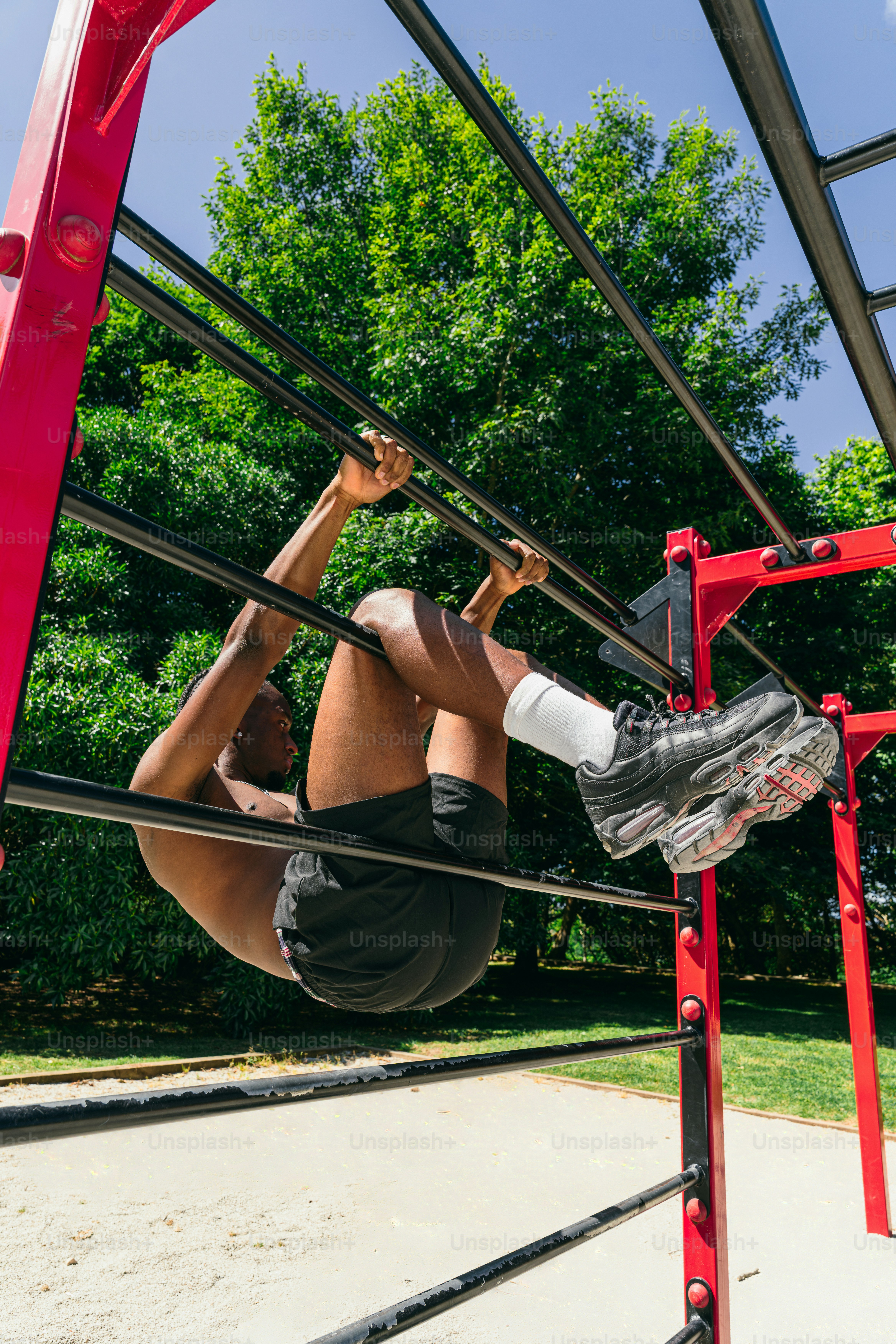 Shirtless man doing crunches on outdoor monkey bars.