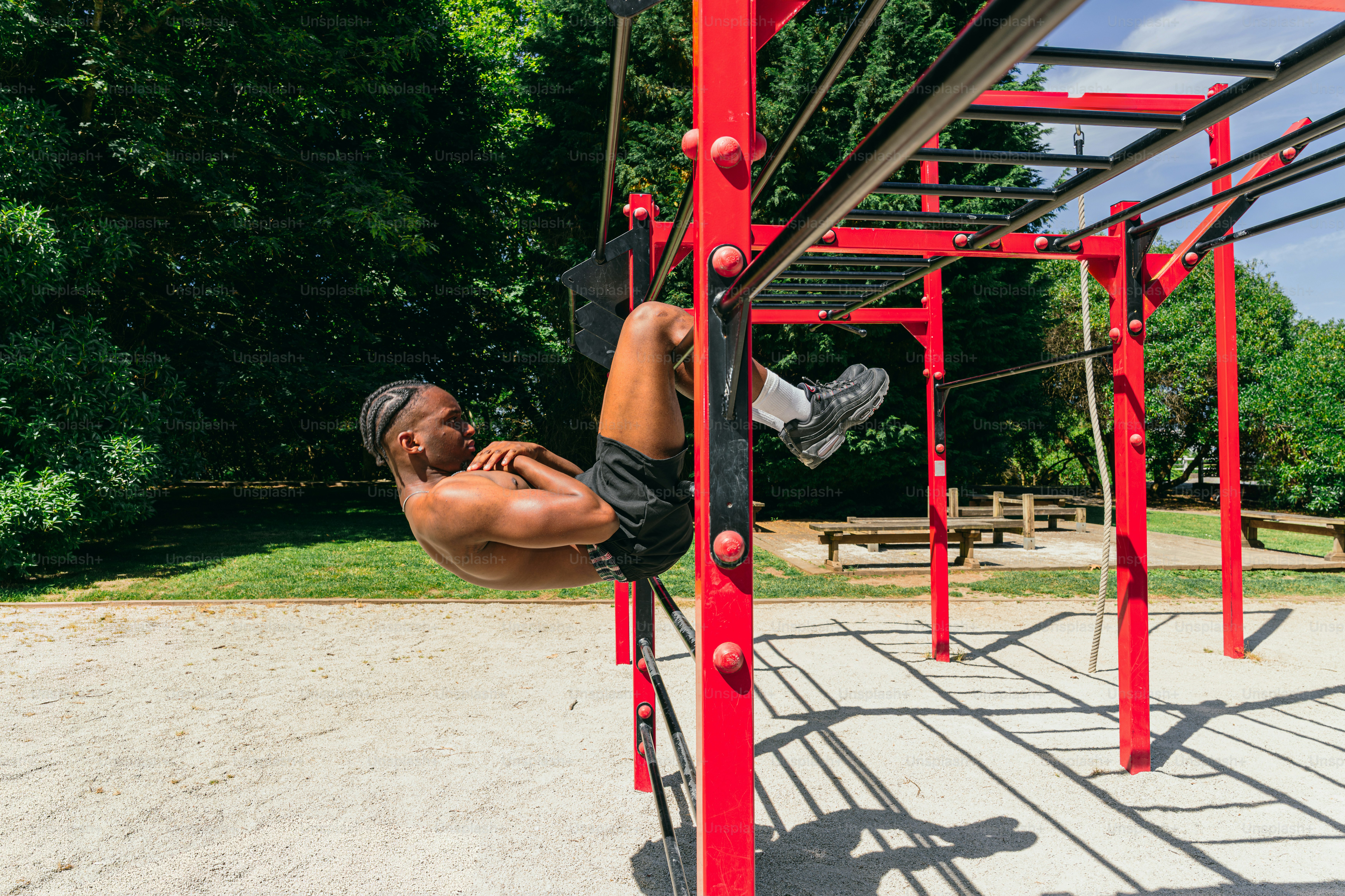 A man exercises on red monkey bars in a park.