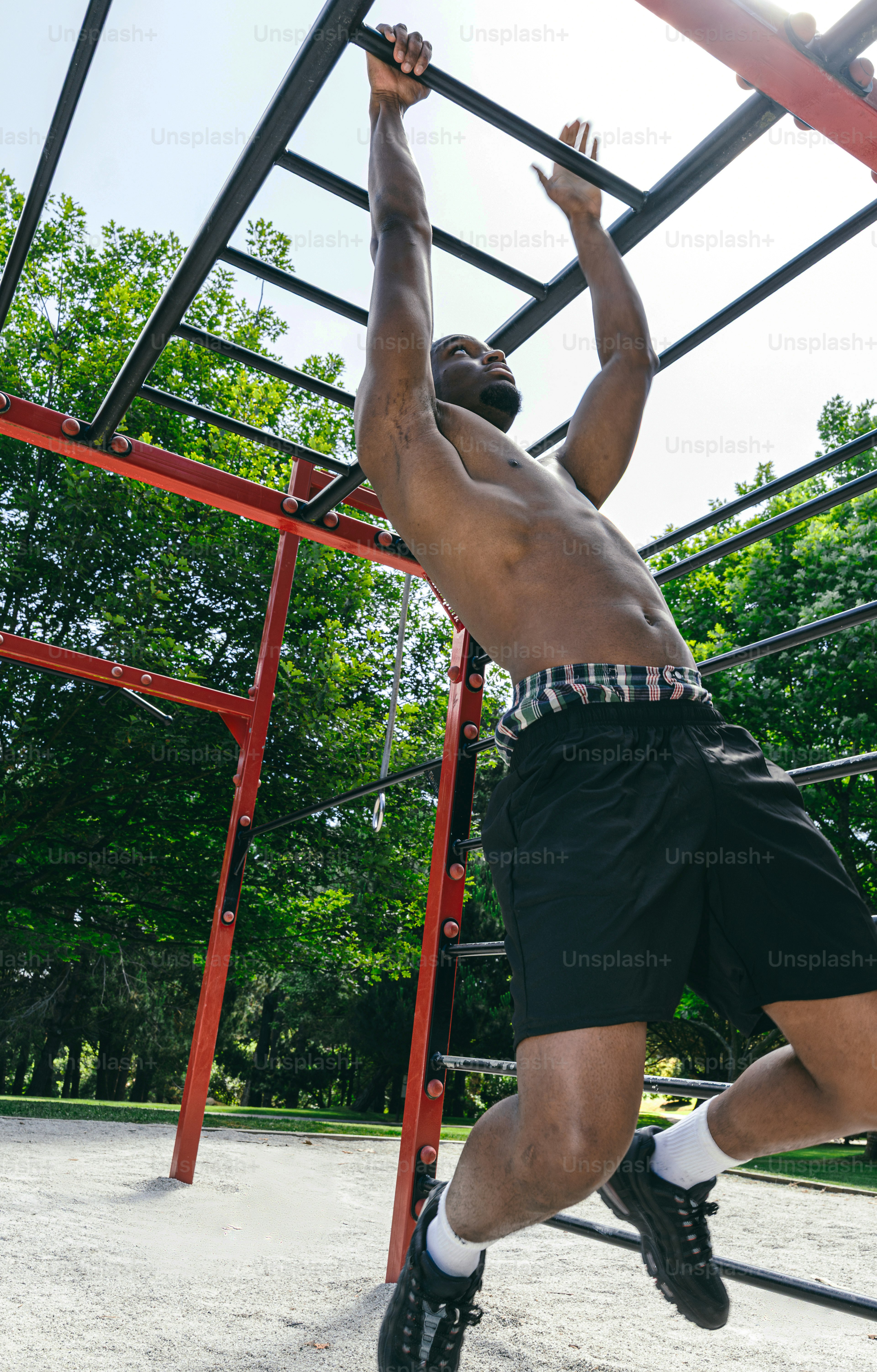 A shirtless man exercises on monkey bars outdoors.