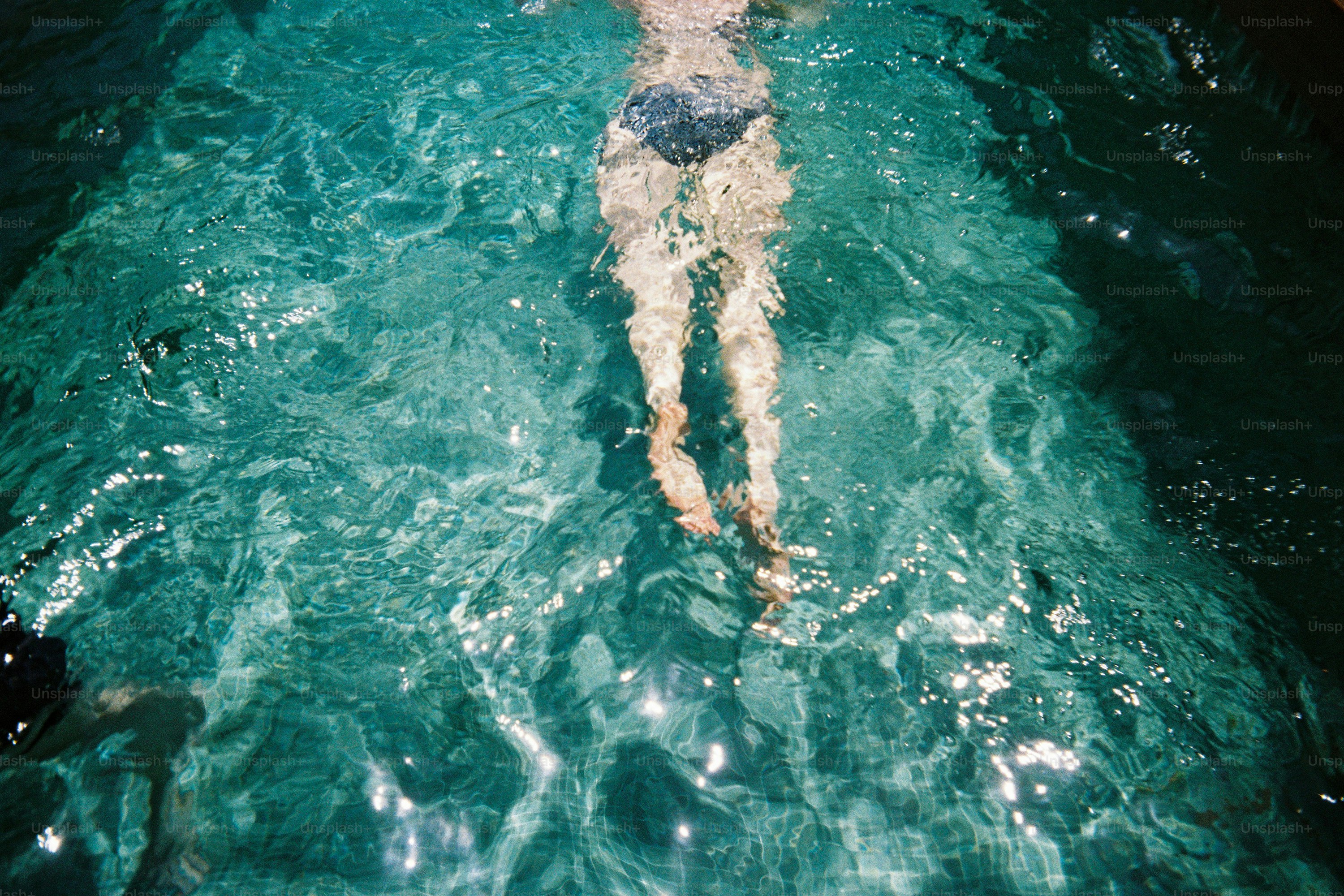 Die Beine einer Person schwimmen im klaren türkisfarbenen Wasser.