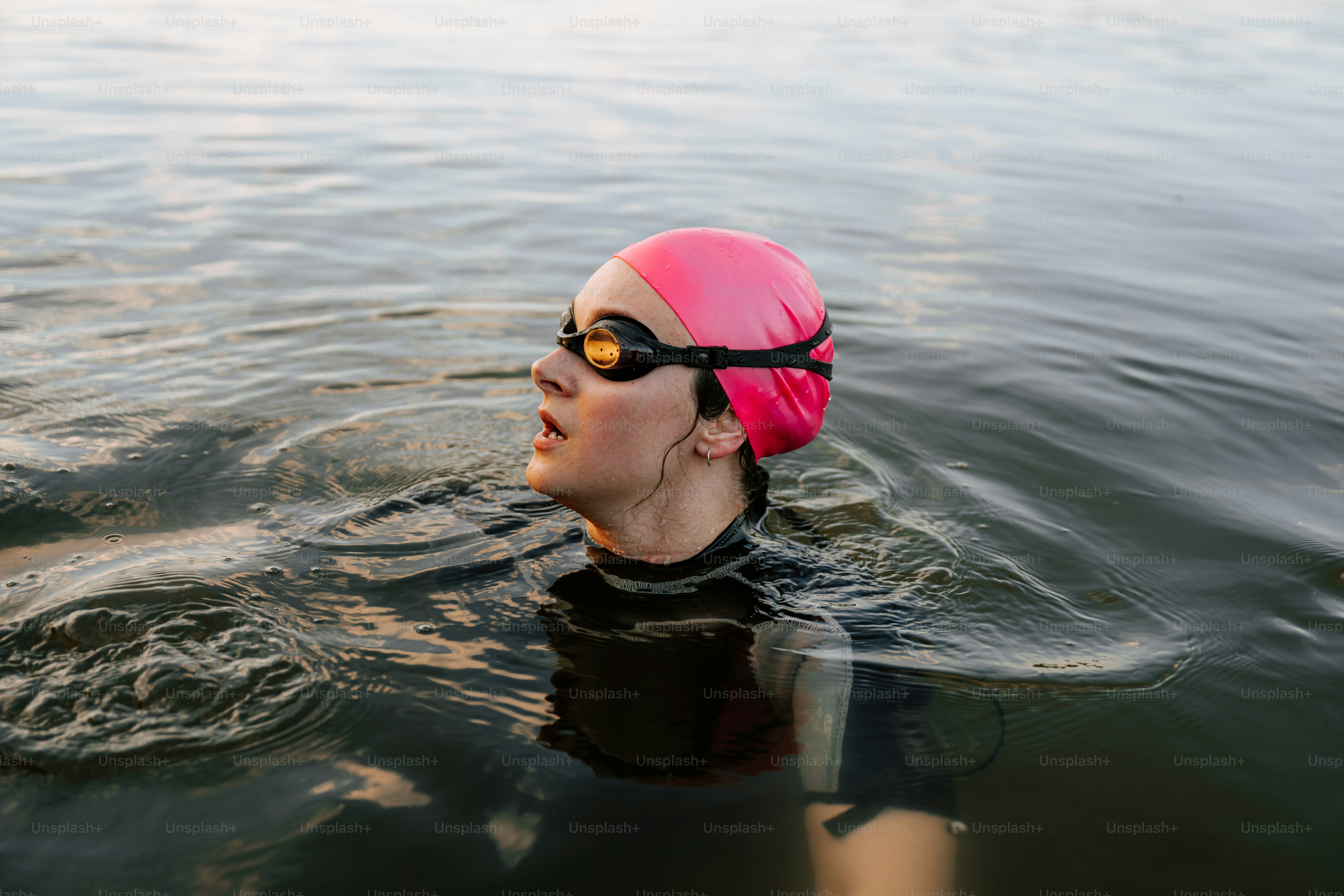 Femme en bonnet de bain rose et lunettes dans l’eau.