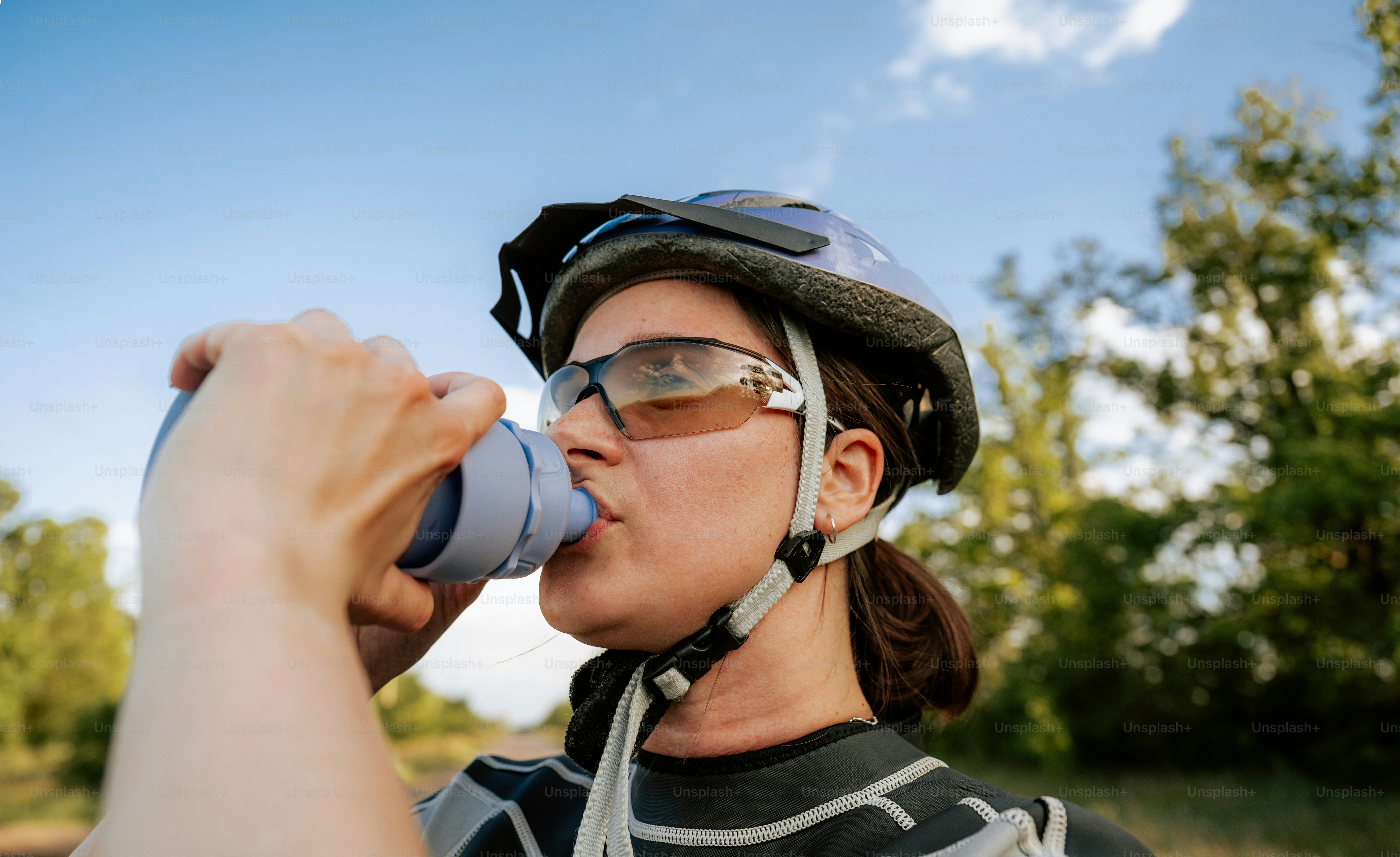 Cycliste portant casque et lunettes boit de l’eau dehors.