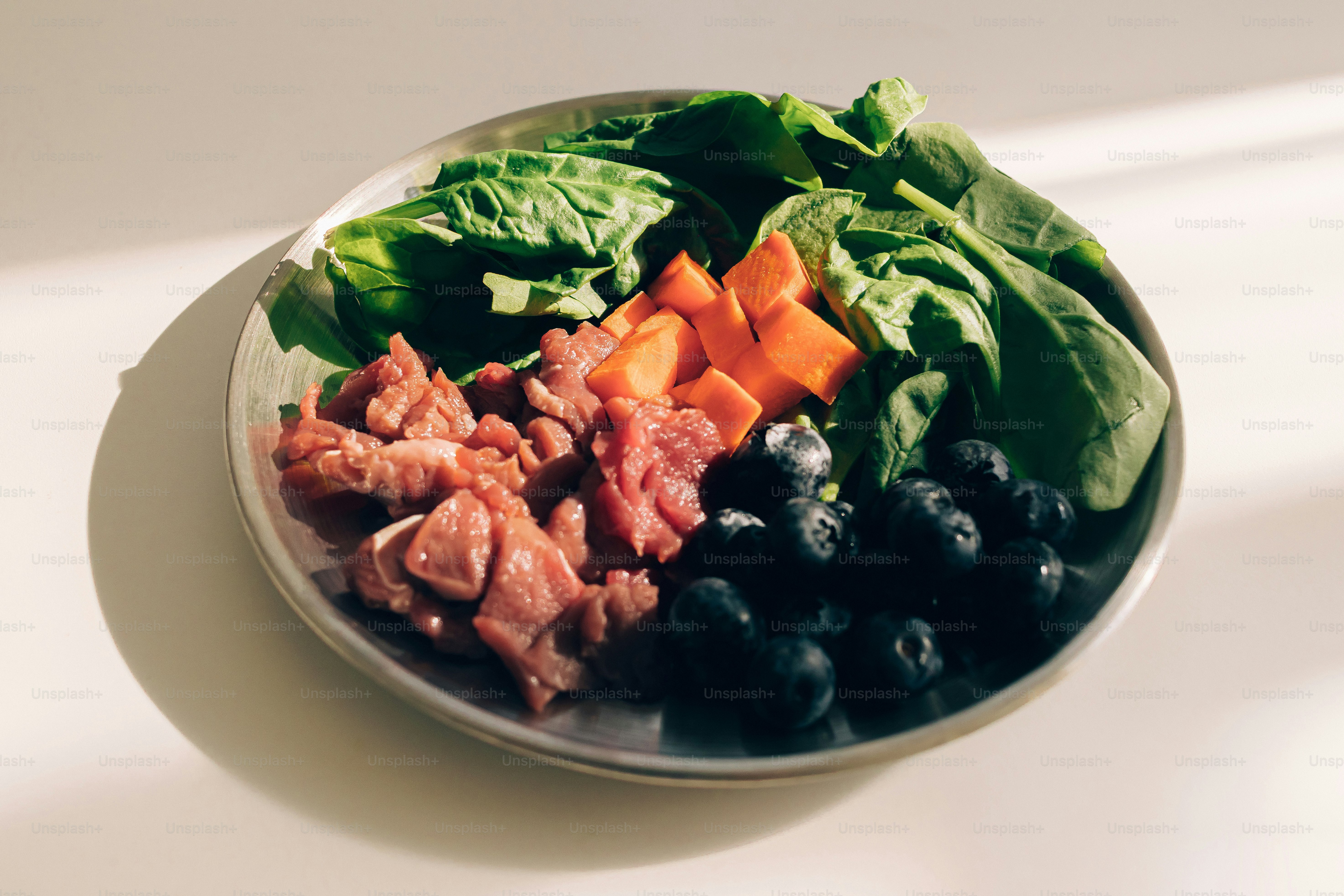 Carne cruda, spinaci, patata dolce e mirtilli in una ciotola.