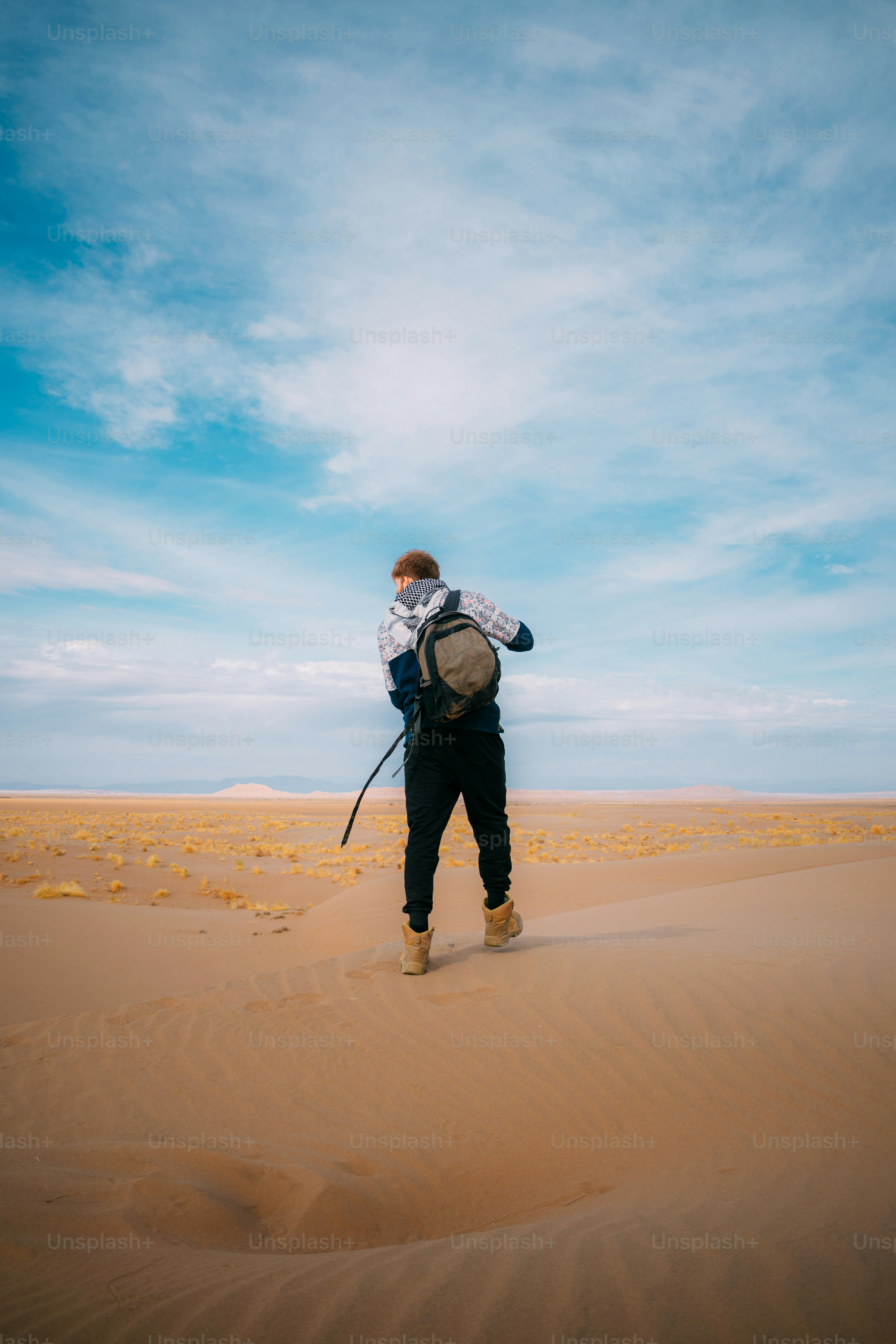 A person walks on desert sand dunes with a backpack