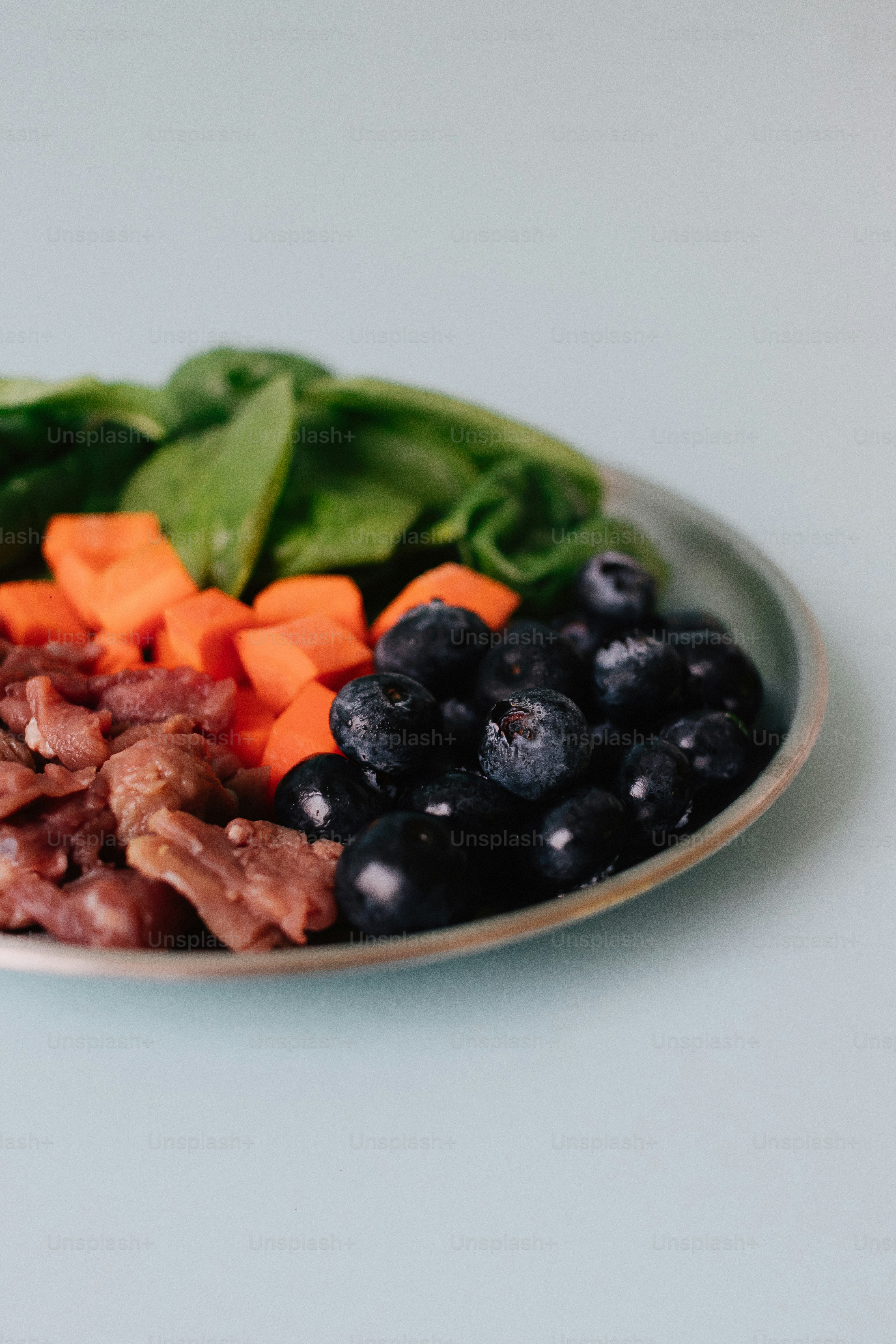 Piring dengan bayam, wortel, blueberry, dan daging.